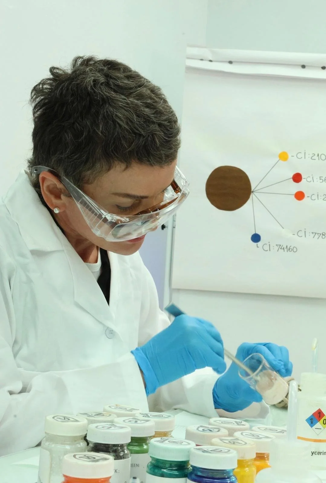 A scientist in a laboratory wearing safety goggles and gloves, working with test tubes filled with colorful liquids.