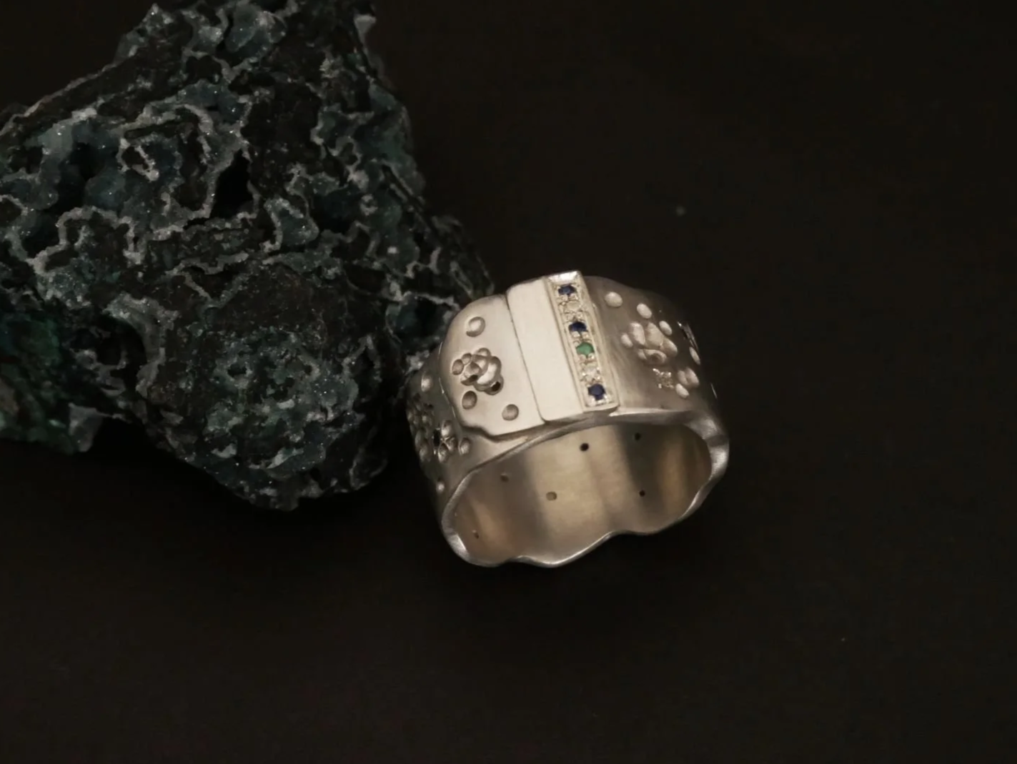 Bague large et originale, sertie de pierres précieuses de couleur bleue et verte. 