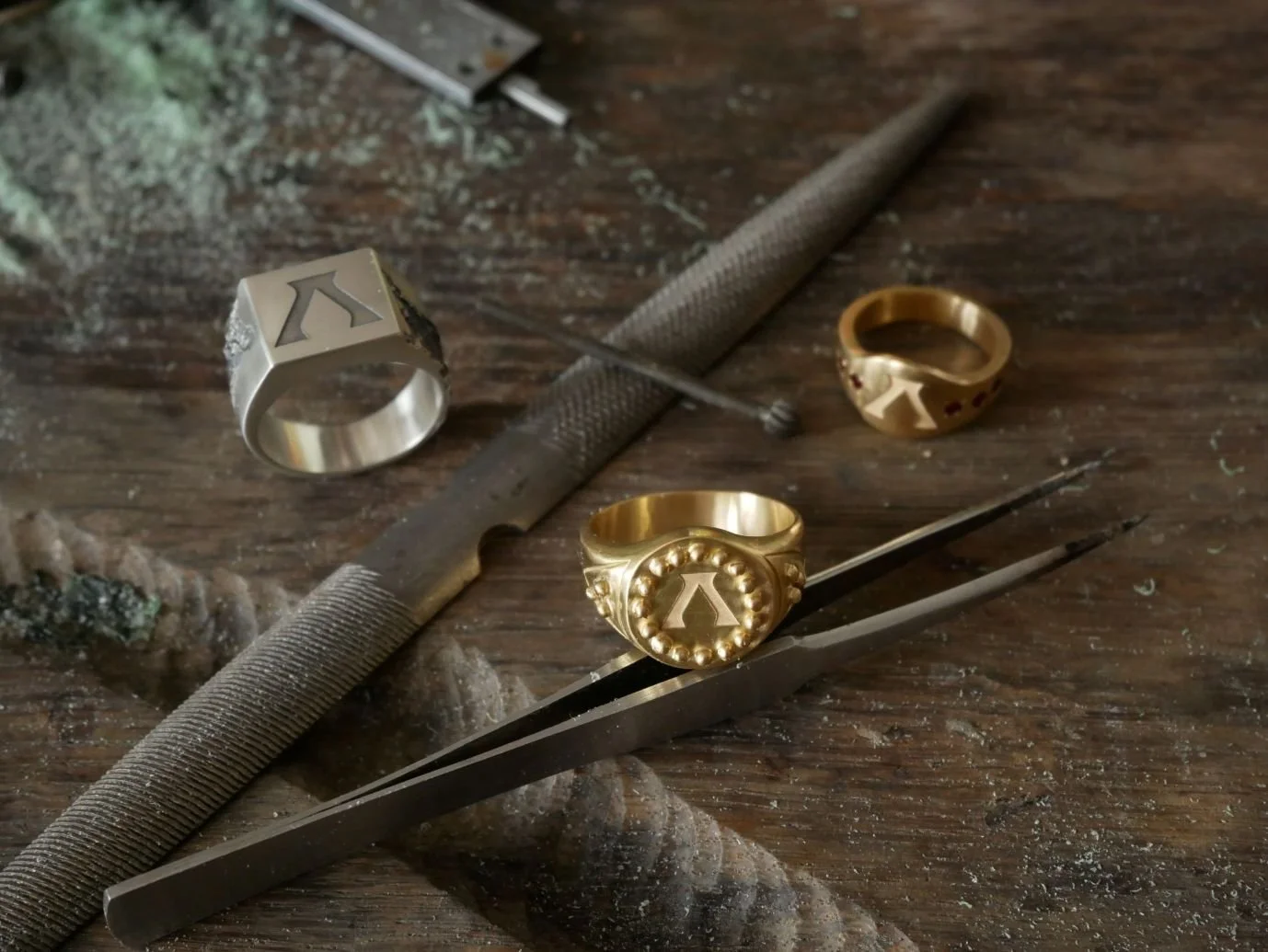 Bagues en or et argent posées sur l'établi, au milieu des outils utilisés pour faire des bijoux faits main.
