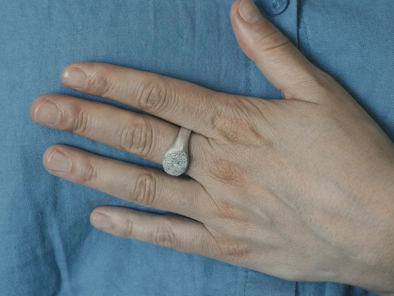 Chevalière avec l’empreinte d’une truffe de chien portée par une femme dont la main est posée sur une chemise bleue.