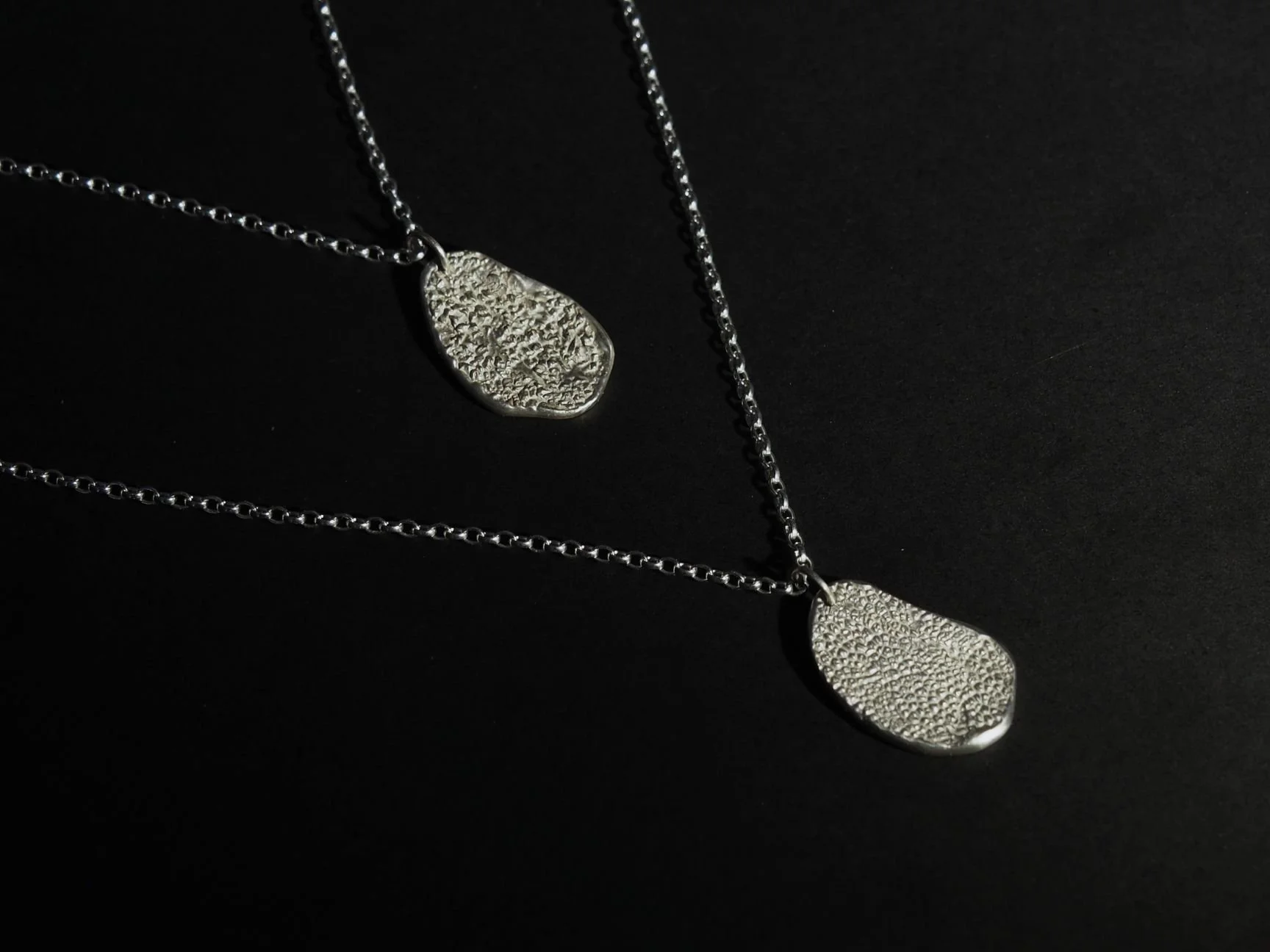 Collier truffe de chien sur mesure. Ce collier est composé de deux pendentifs truffe dont les chaînes se rejoignent pour former un sautoir. Les empreintes sur les colliers ont des textures différentes car il s’agit de races de chiens différentes.
