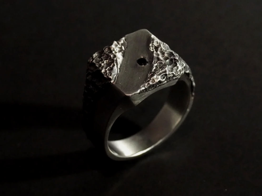 Chevalière en argent avec un jeu de texture sur le plateau sur fond noir.