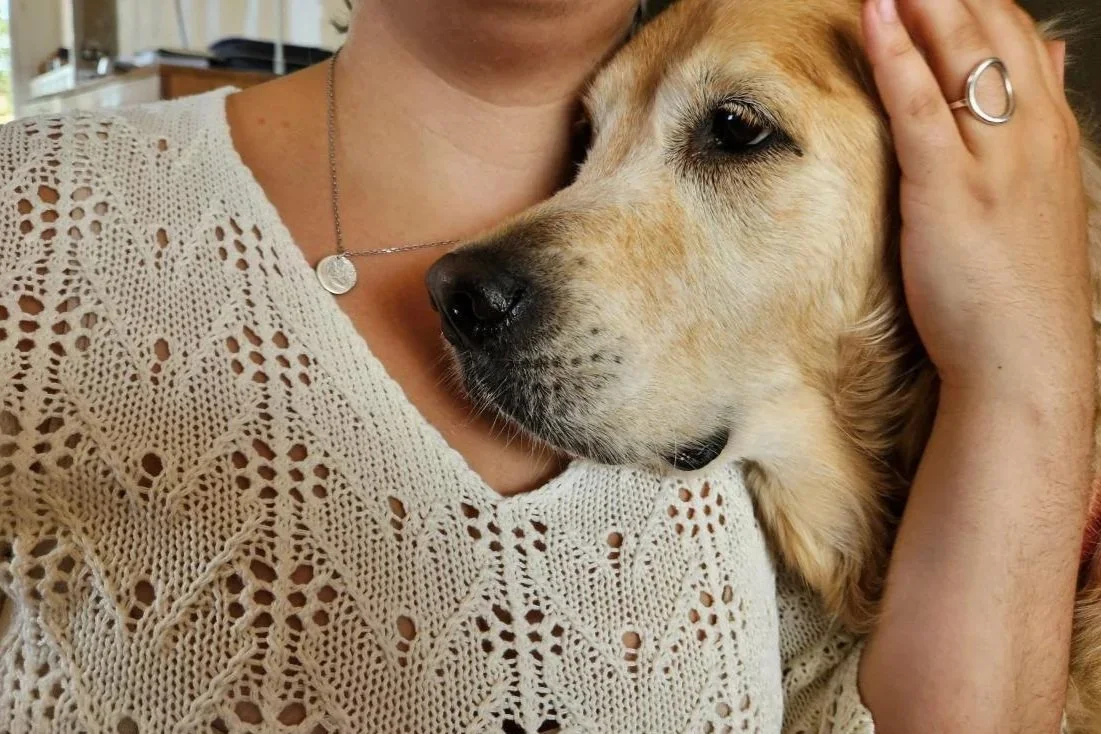 Collier empreinte de chien en argent porté au cou d’une femme. Cette femme fait un câlin à son chien qui a justement prêté l’empreinte de sa truffe pour faire ce bijou.