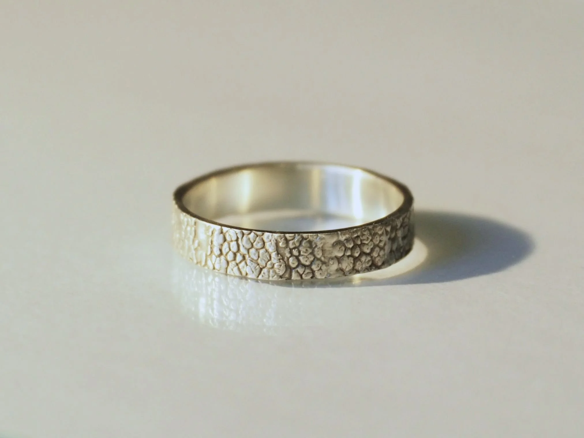 Une bague lumineuse posée sur une surface blanche révèle un motif de truffe gravé tout autour. Bague empreinte truffe chien élégante et raffinée, création sur mesure alliant émotion et savoir faire artisanal.