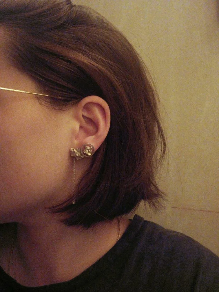 Oreille d’une jeune femme portant deux boucles d’oreilles Atelier 962° : pendante en argent recyclé et puce minimaliste. Créations artisanales lyonnaises mêlant textures brutes et design asymétrique raffiné.