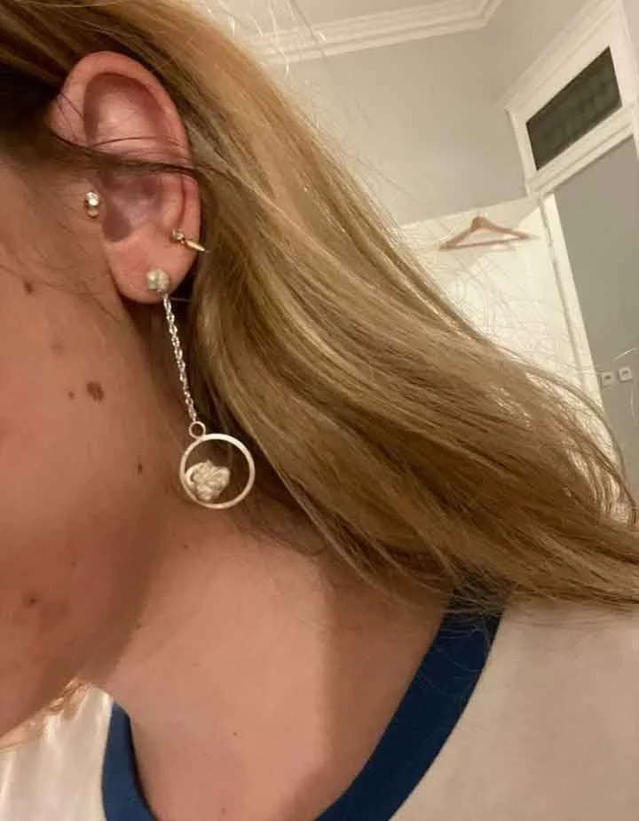 Boucles d’oreilles pendantes en argent recyclé portées par une jeune femme blonde. La forme circulaire ajourée révèle un travail manuel précis typique de l’atelier de bijouterie artisanale à Lyon.