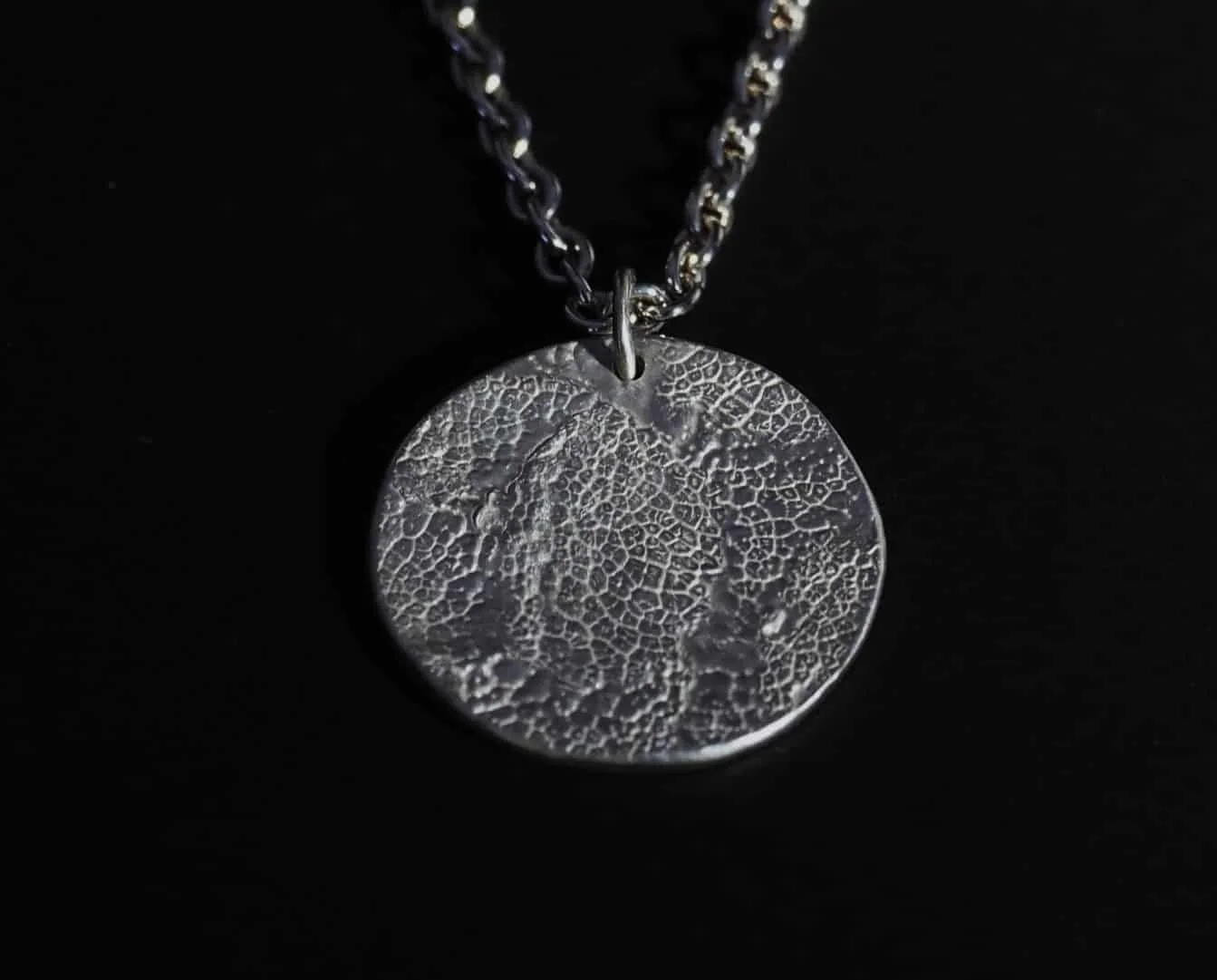 collier empreinte de chien avec une chaîne en argent sur fond noir. C’est un bijou souvenir de son chien, idéal comme cadeau pour un maître ou une maîtresse de chien.
