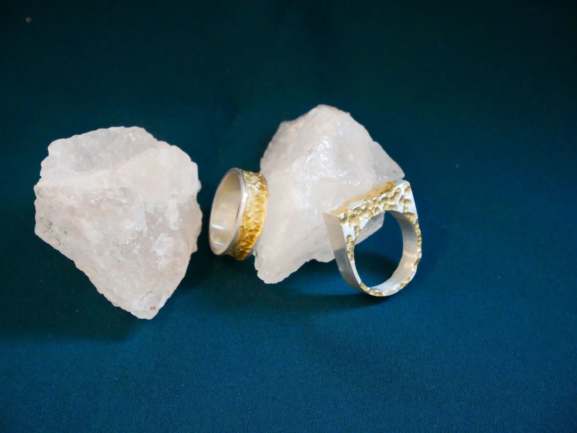 Une bague or et argent et une bague carrée or et argent, sur caillou blanc translucide et fond bleuté. Mélange de métaux précieux, pièces uniques de créateur.