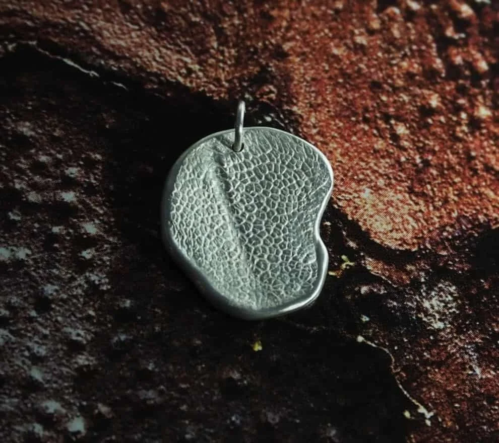 pendentif truffe de chien sur un fond ocre. Ce bijou avec l’empreinte de votre animal est en argent 925 avec des finitions mates. Ce collier truffe n’est pas rond, c’est une commande sur mesure. L’empreinte de la truffe se distingue nettement.