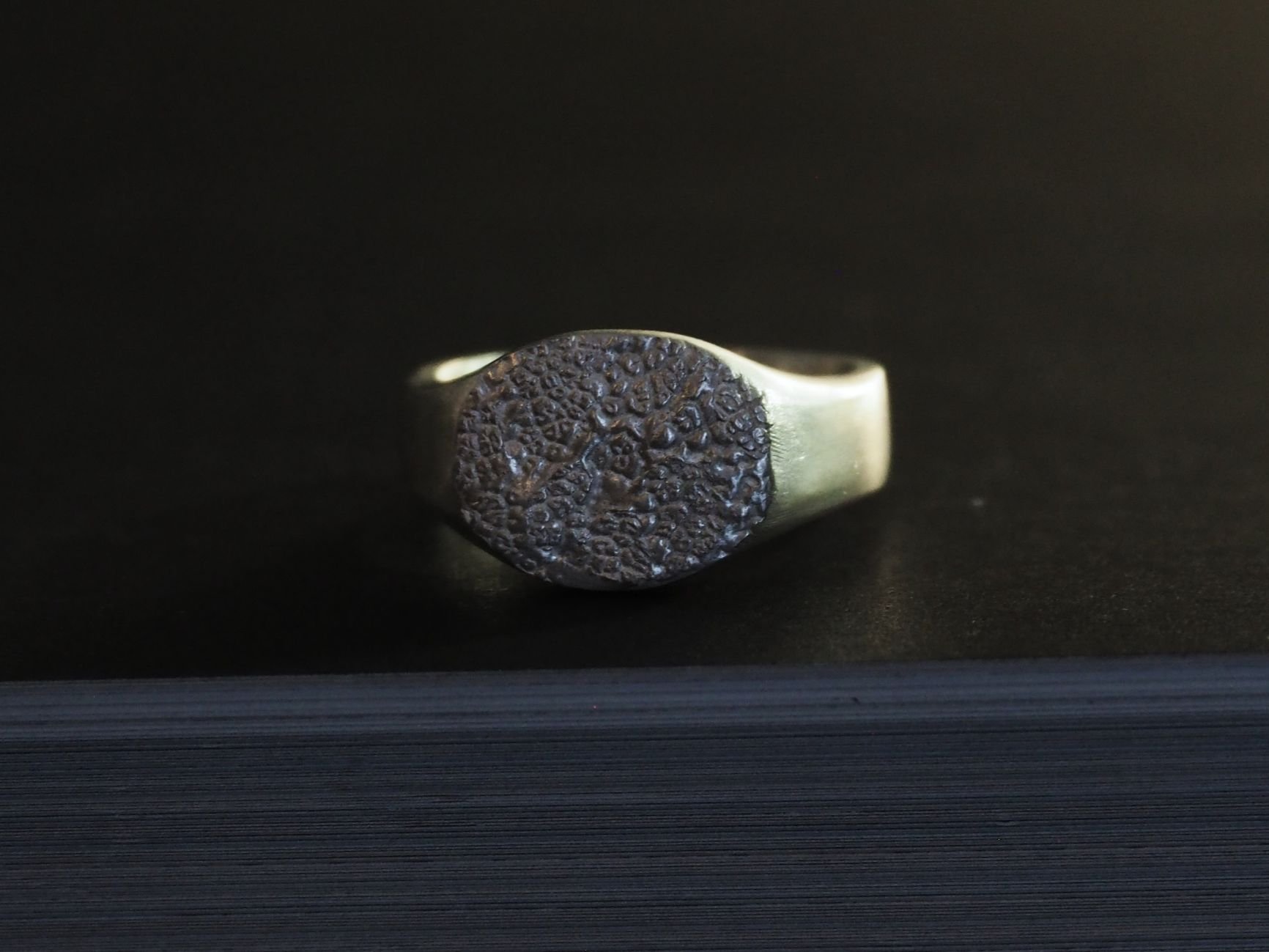Chevalière truffe de chien en argent posée sur un fond noir. Cette chevalière est idéale lorsqu’on souhaite porter une grosse bague empreinte truffe de chien.