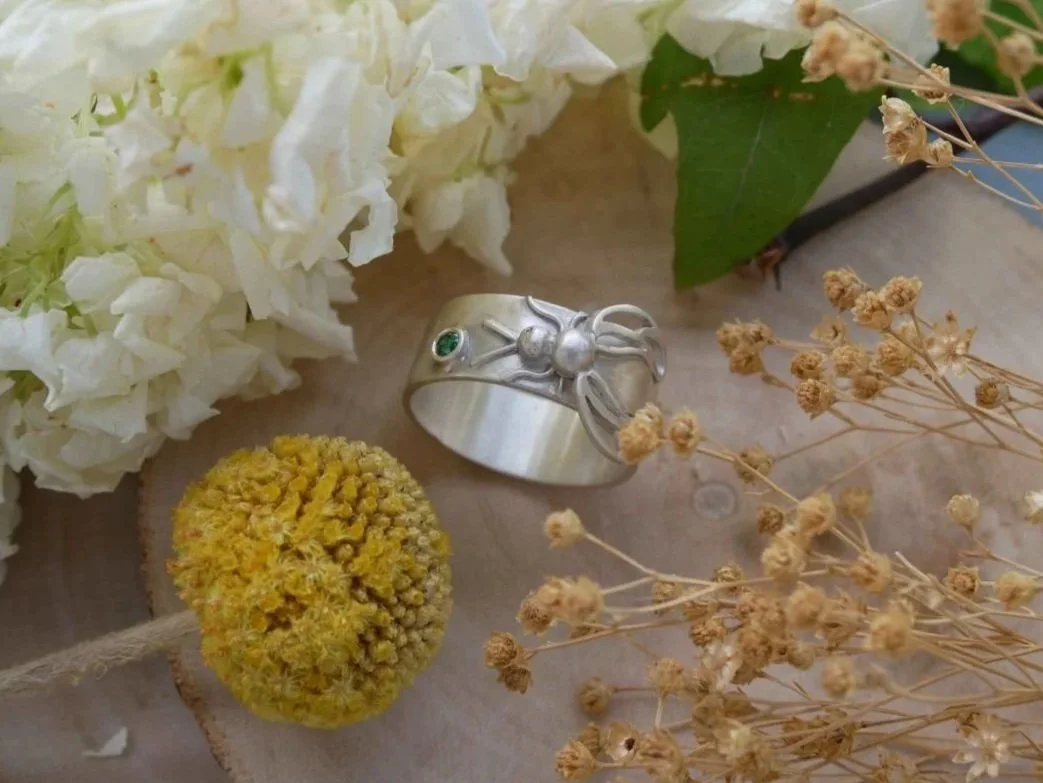 Bague sur mesure avec une abeille en argent sculptée sur le métal  qui butine une pierre verte. 