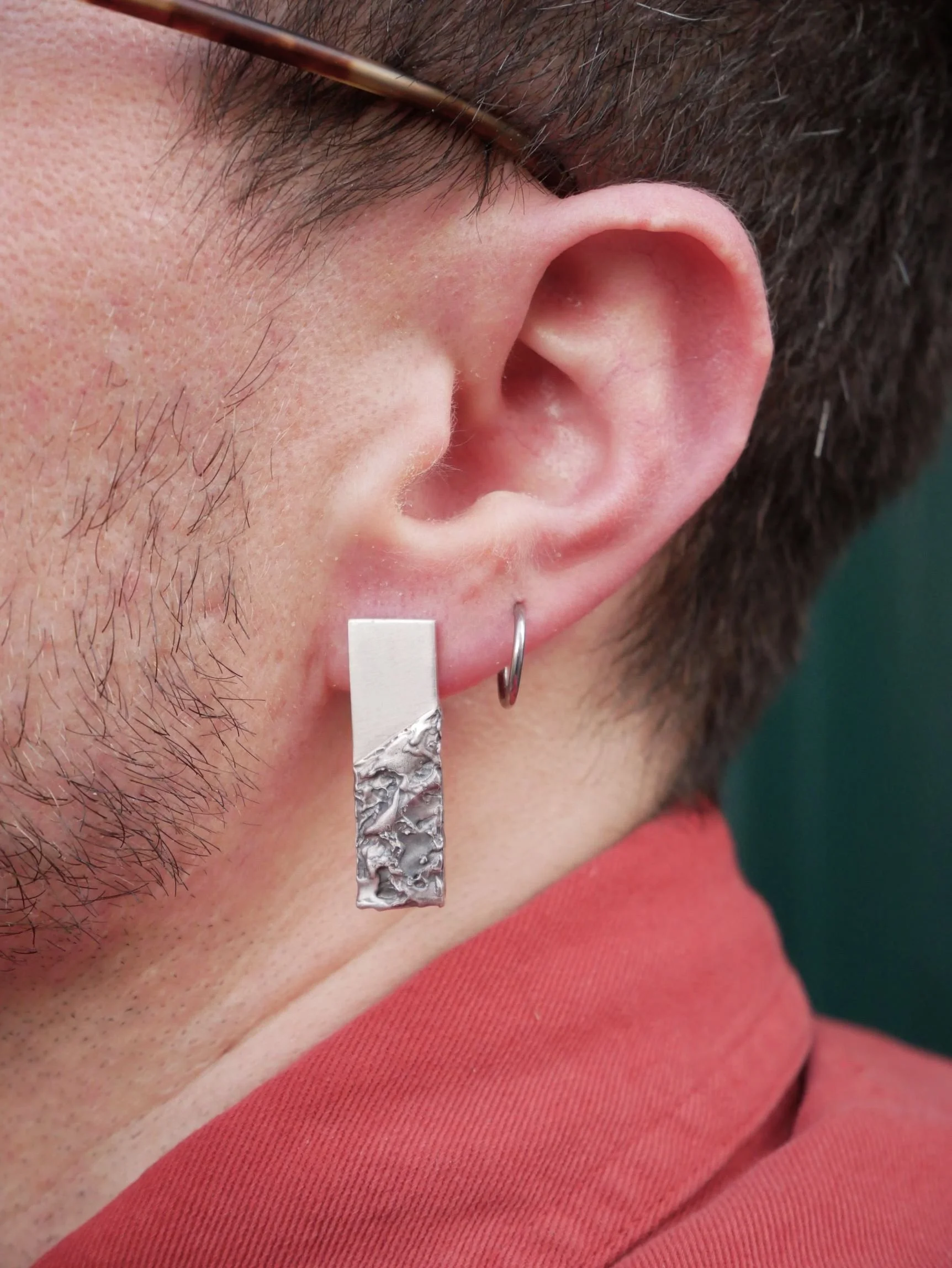 Boucles d’oreilles en argent portées par un homme : partie brillante polie et texturée oxydée. Bijoux masculins audacieux en argent massif, style contemporain.