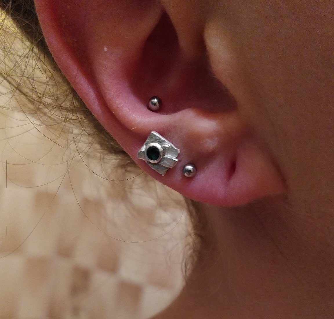 Puce d’oreille toute petite en argent recyclé sertie d’une émeraude, collée à l’oreille d’une cliente fidèle. Commande sur-mesure discrète et raffinée réalisée à la main dans un atelier lyonnais.