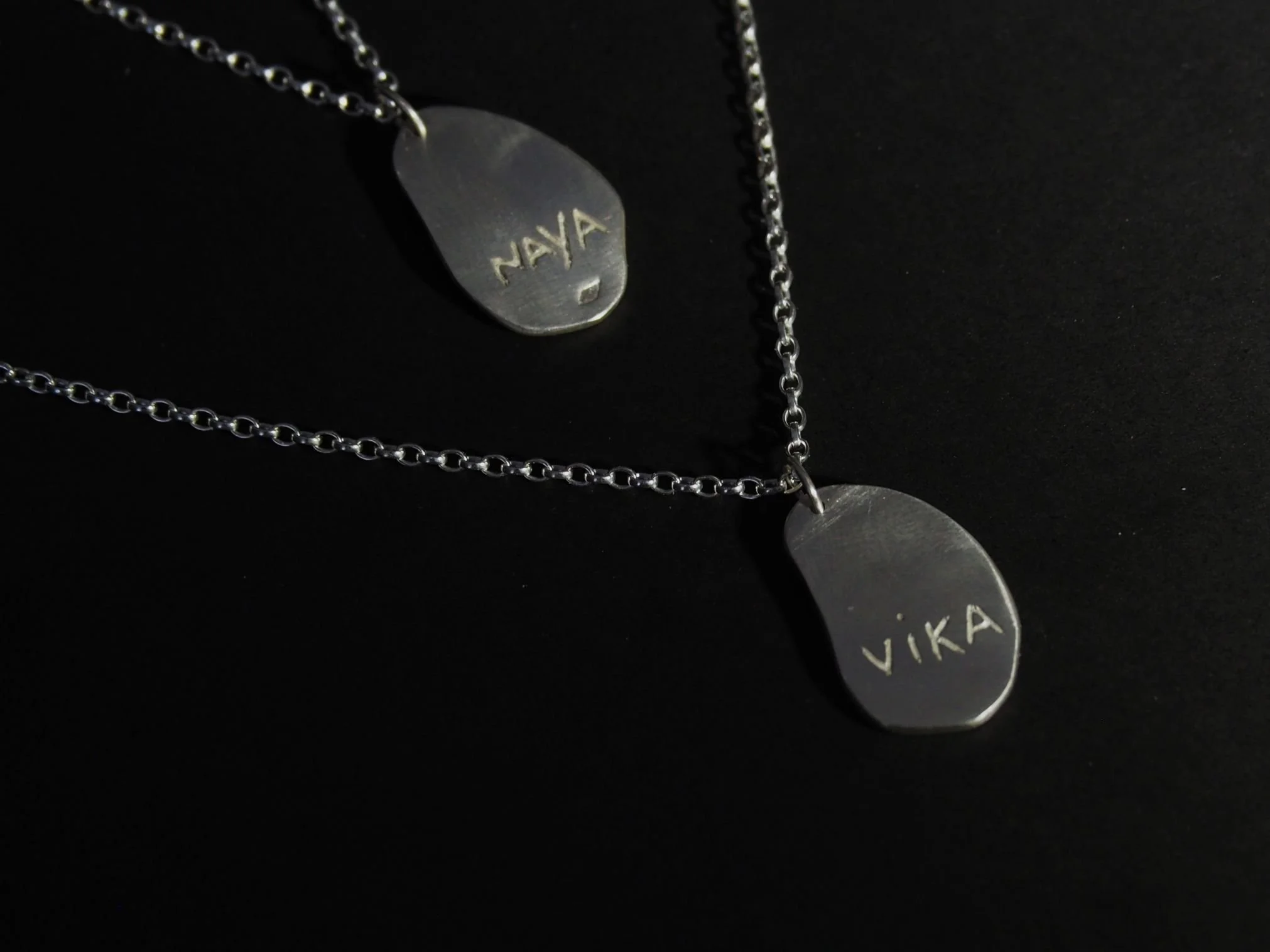 Collier empreinte de chien sur mesure composé de deux pendentifs truffe de chien en argent. Lorsqu’on retourne le bijou, on aperçoit, associé à chaque pendentif truffe, le prénom du chien gravé dans le métal.