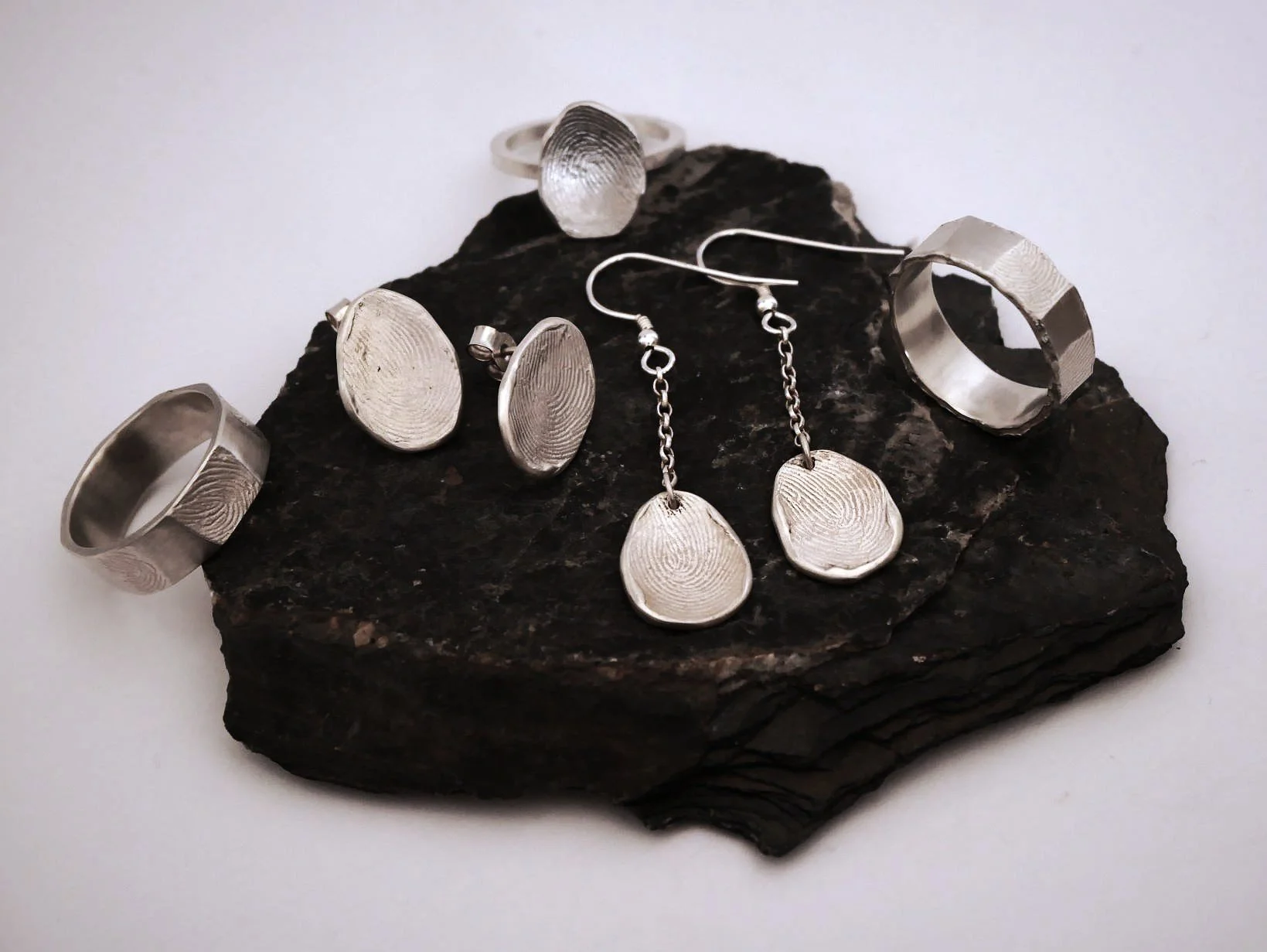 Des bijoux empreintes digitales posés sur une pierre et sur un fond blanc.