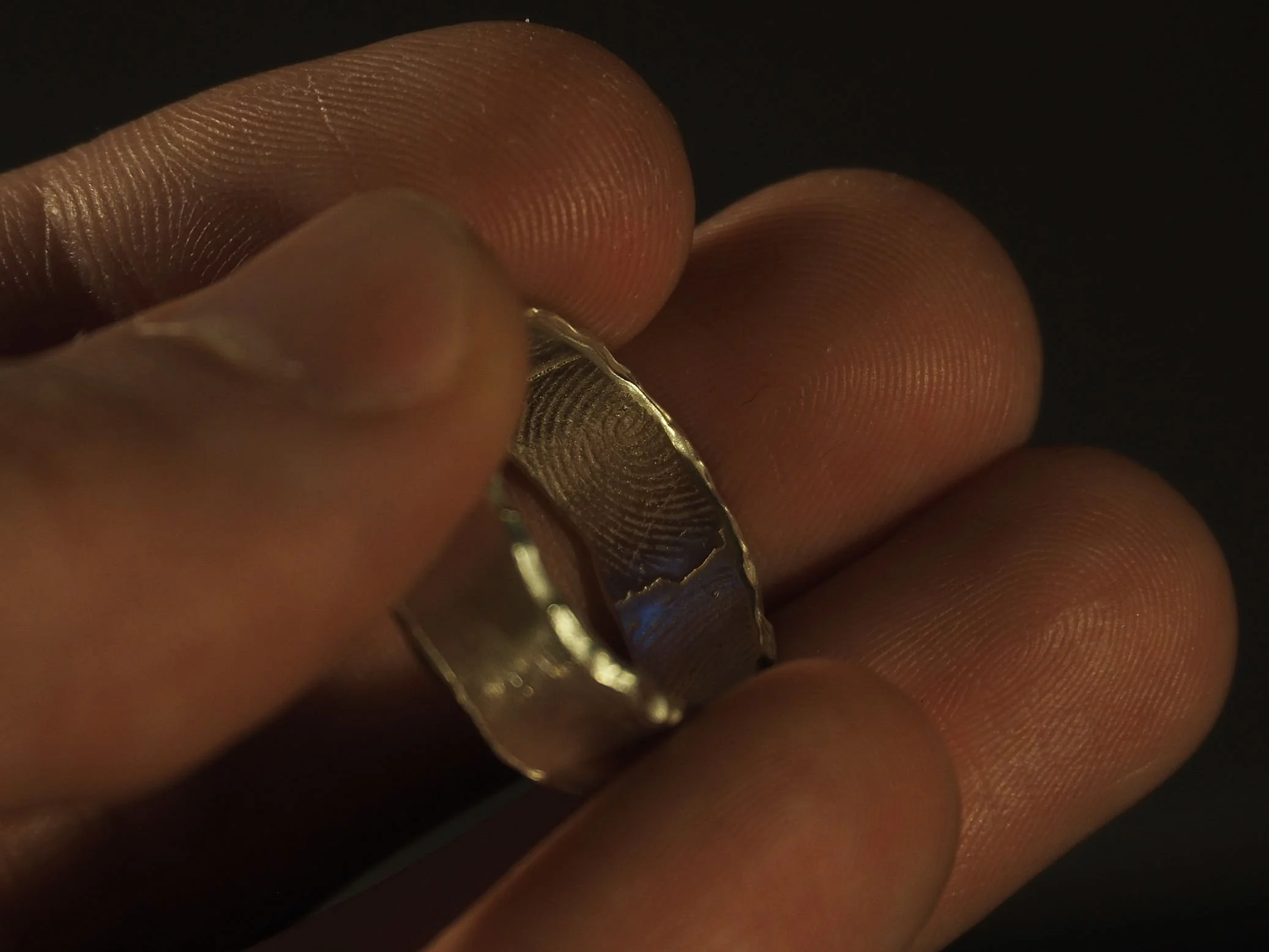 Bague empreinte digitale en argent tenue entre des doigts, rebord fondu et finition lisse, bijou empreinte sur-mesure signé Atelier 962°, symbole d’émotion, d’attachement et d’histoire unique.