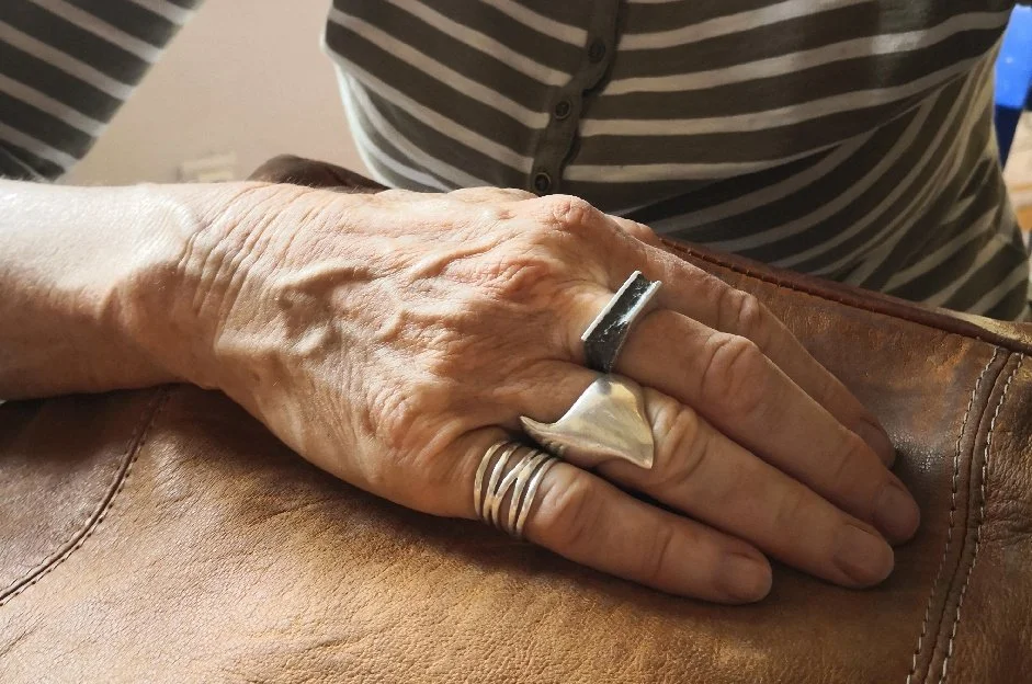 Gros plan sur la main d’une femme âgée portant une bague carrée en argent massif texturé, posée sur son sac en cuir. Moderne et géométrique, cette création artisanale lyonnaise mêle lignes brutes et savoir-faire français.