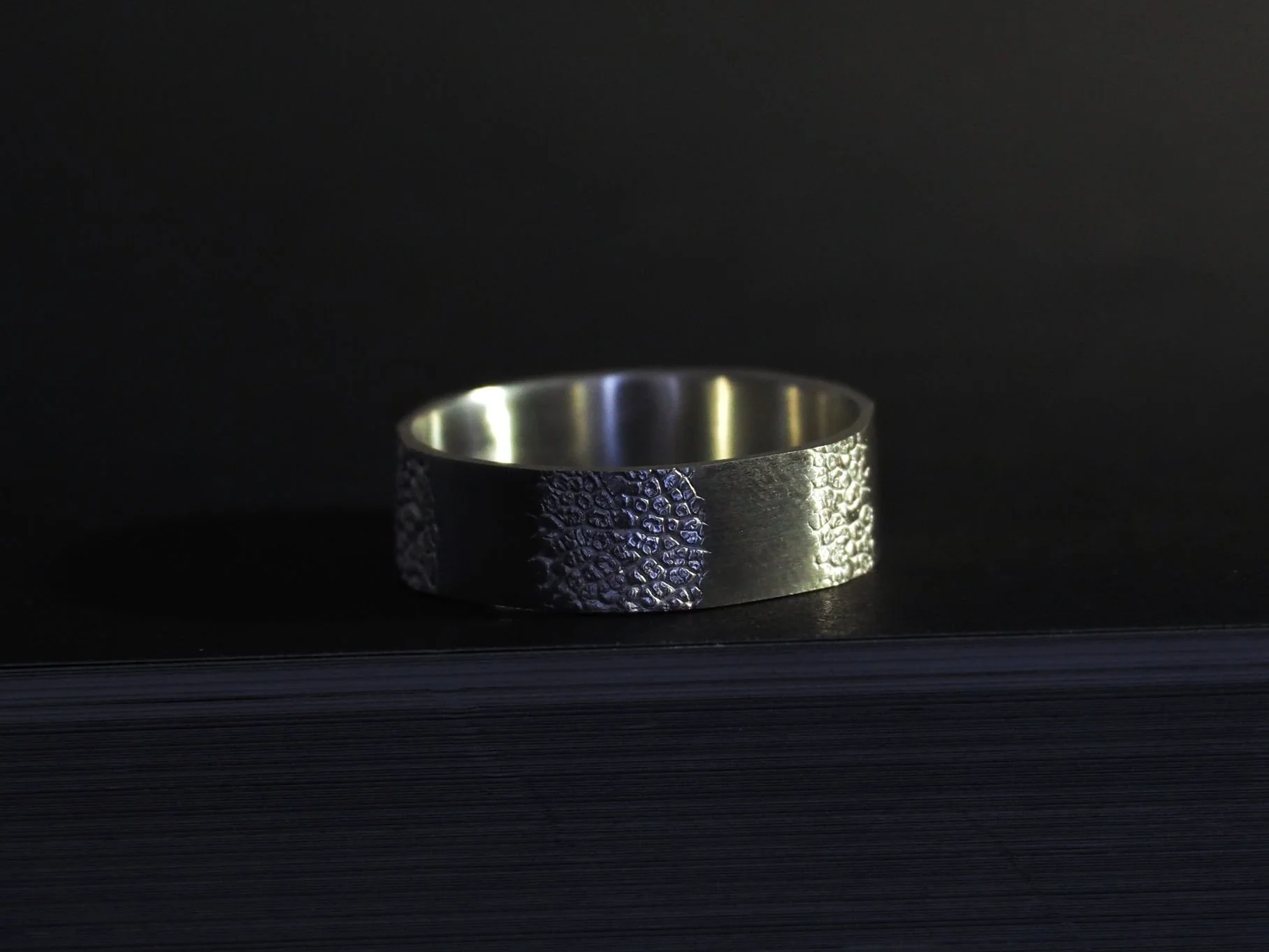 Bague truffe de chien sur fond noir. Cet anneau est composé de plusieurs facettes sur lesquelles apparaît plusieurs fois l’empreinte de truffe d’un chien.
