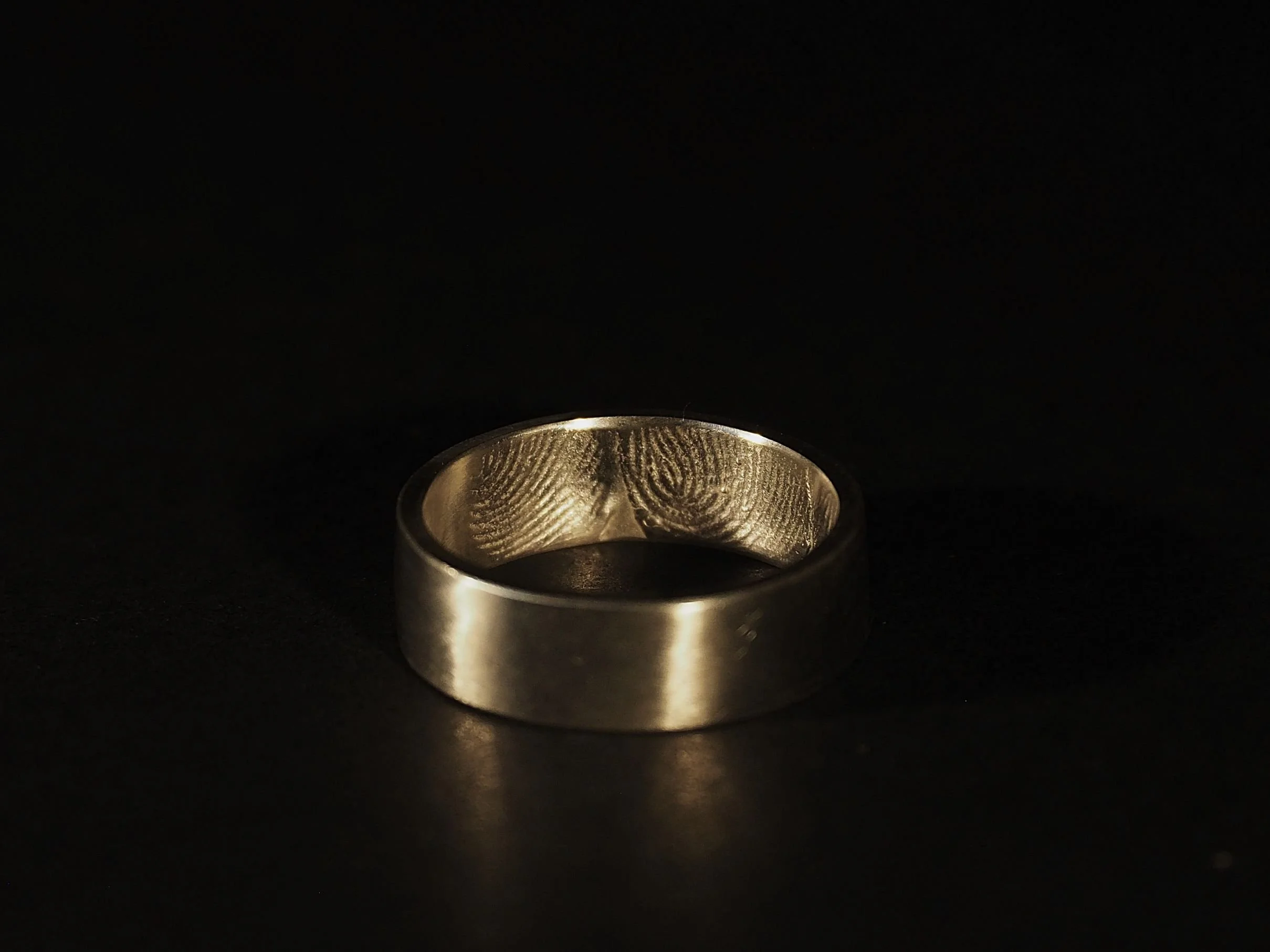 Bague empreinte en argent à rebord lisse posée sur fond noir, bijou sentimental et sur-mesure gravé à l’intérieur, création artisanale lyonnaise Atelier 962°, symbole d’un lien intemporel.