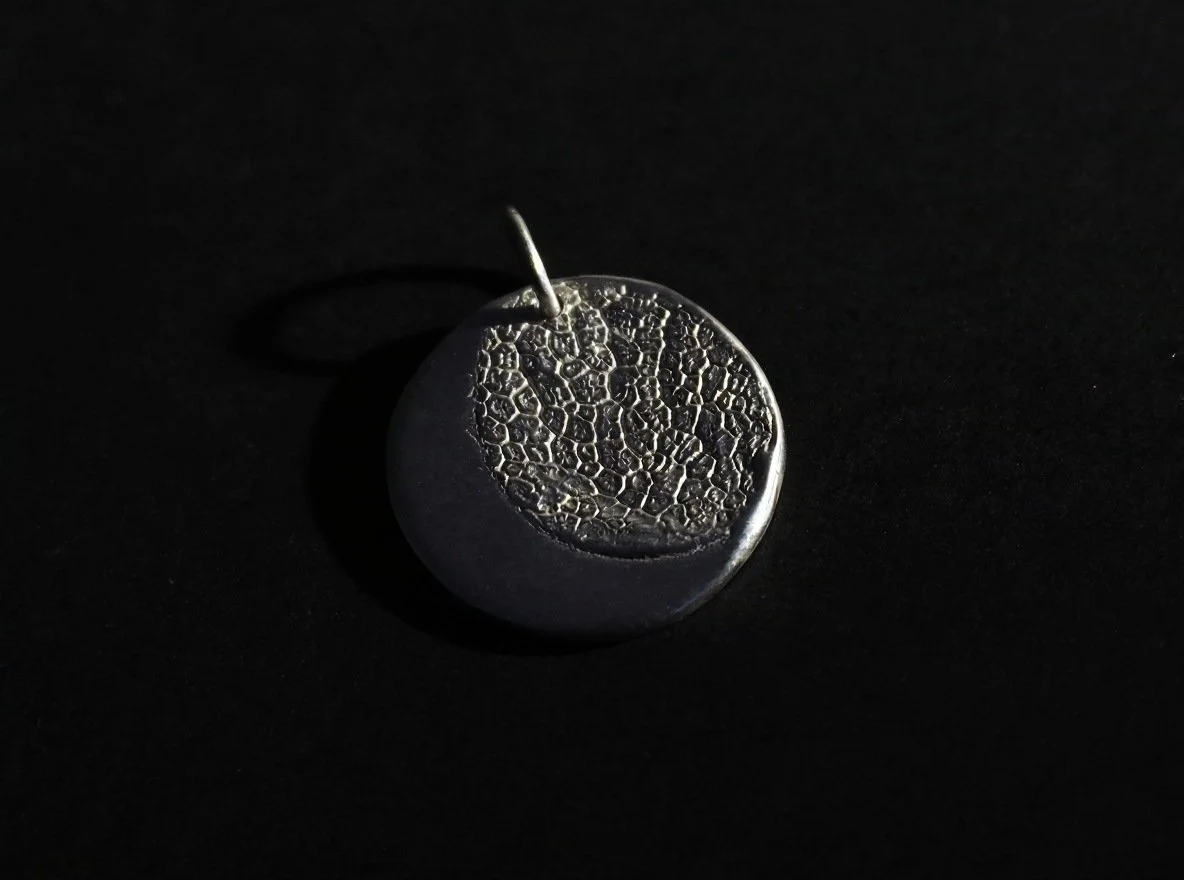 Pendentif avec l’empreinte d’un chien sur fond noir. C’est un collier truffe sur mesure, laissant apparaître un croissant de lune.