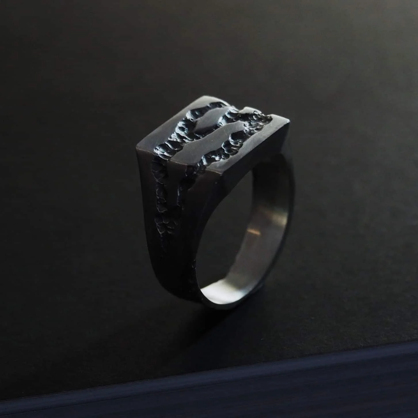 Chevalière en argent sur mesure sur fond noir.