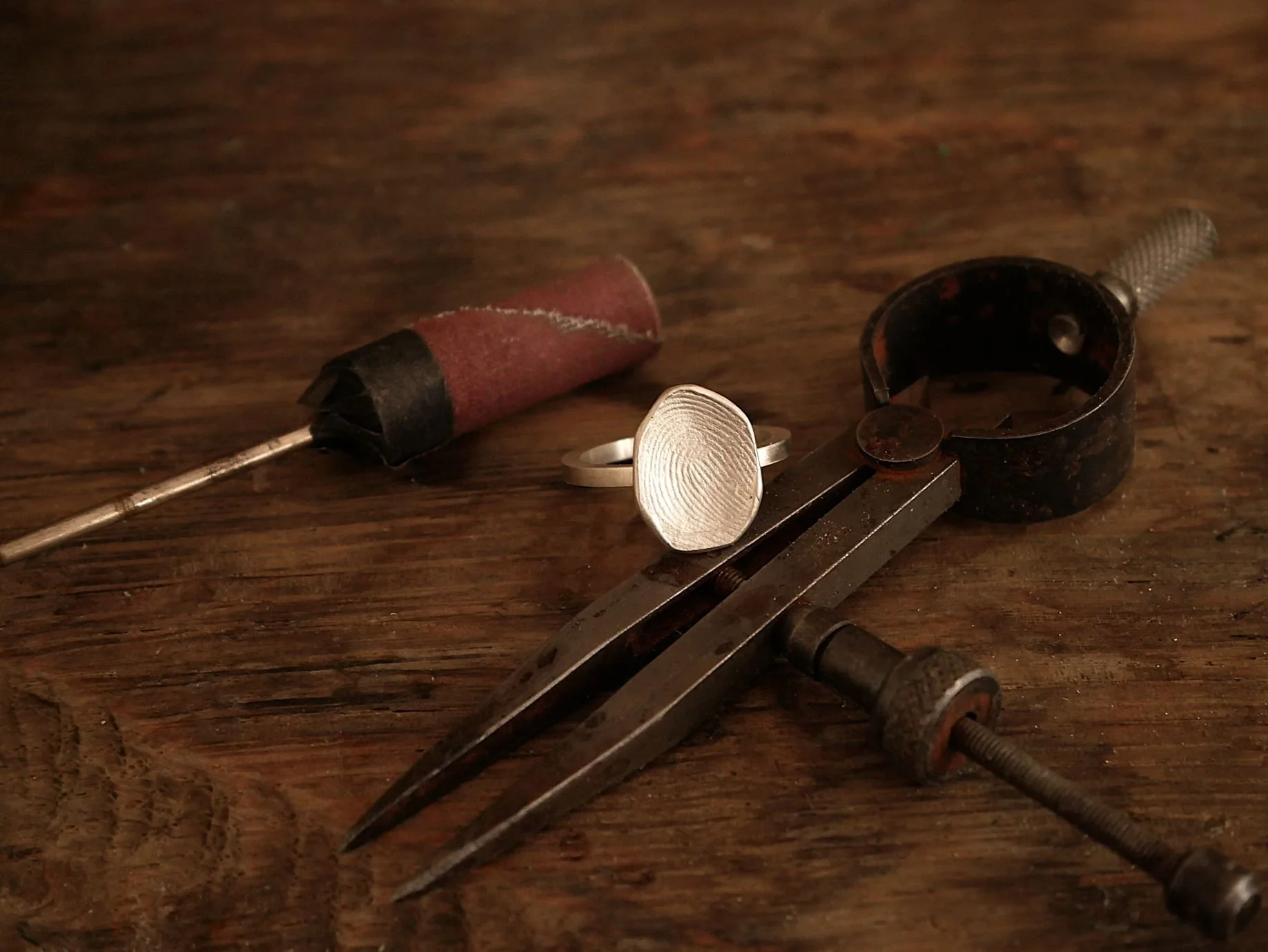 Bague empreinte de doigt en argent posée sur établi de bijoutière, entourée d’outils d’artisanat, bijou sur-mesure incarnant l’émotion, le savoir-faire et la beauté symbolique d’une création unique.