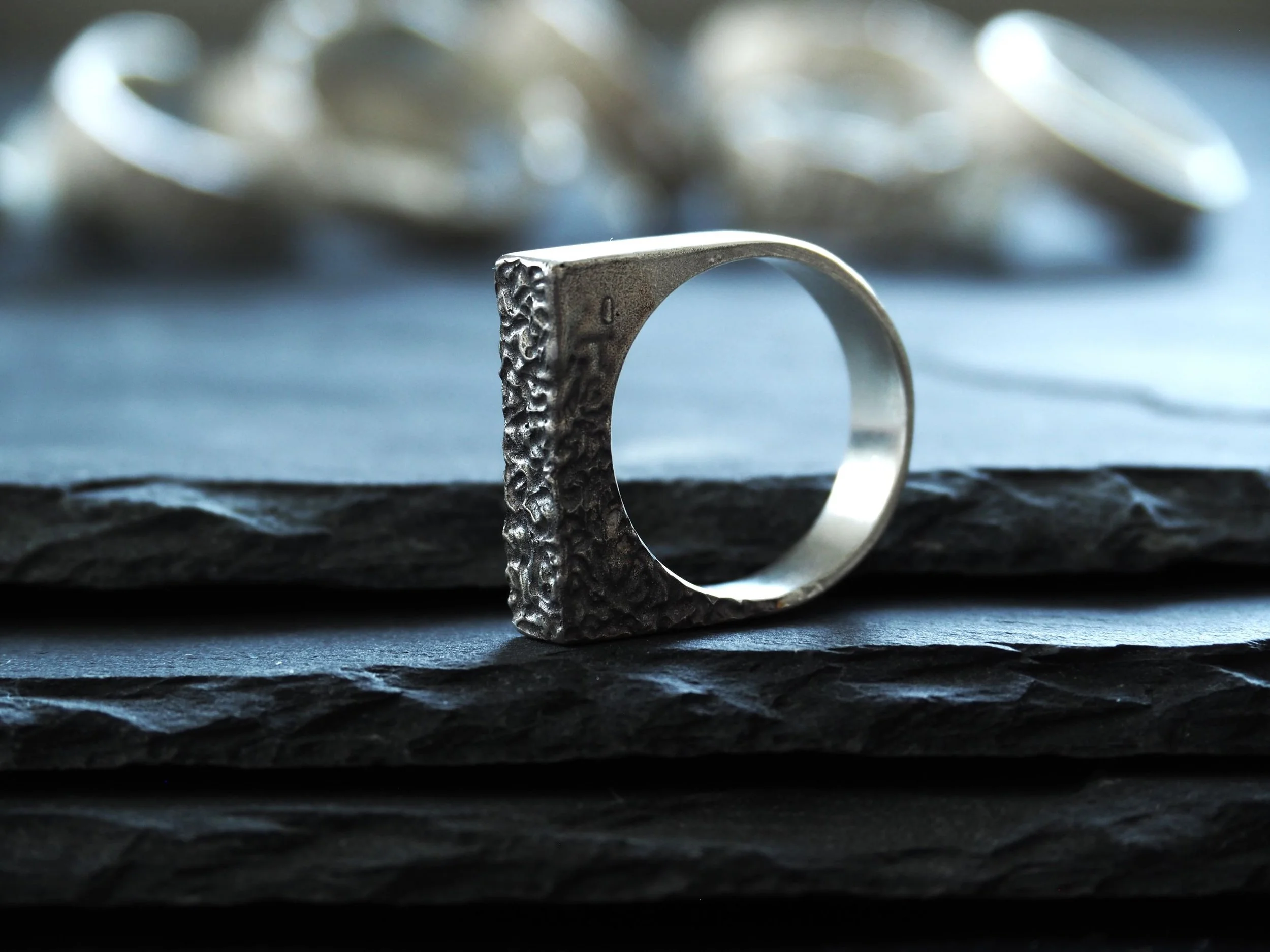 Bague carrée en argent massif reposant sur ardoises texturées. Design géométrique, bague argent large et contemporaine, parfaite pour homme ou femme en quête de grosse bague en argent originale.