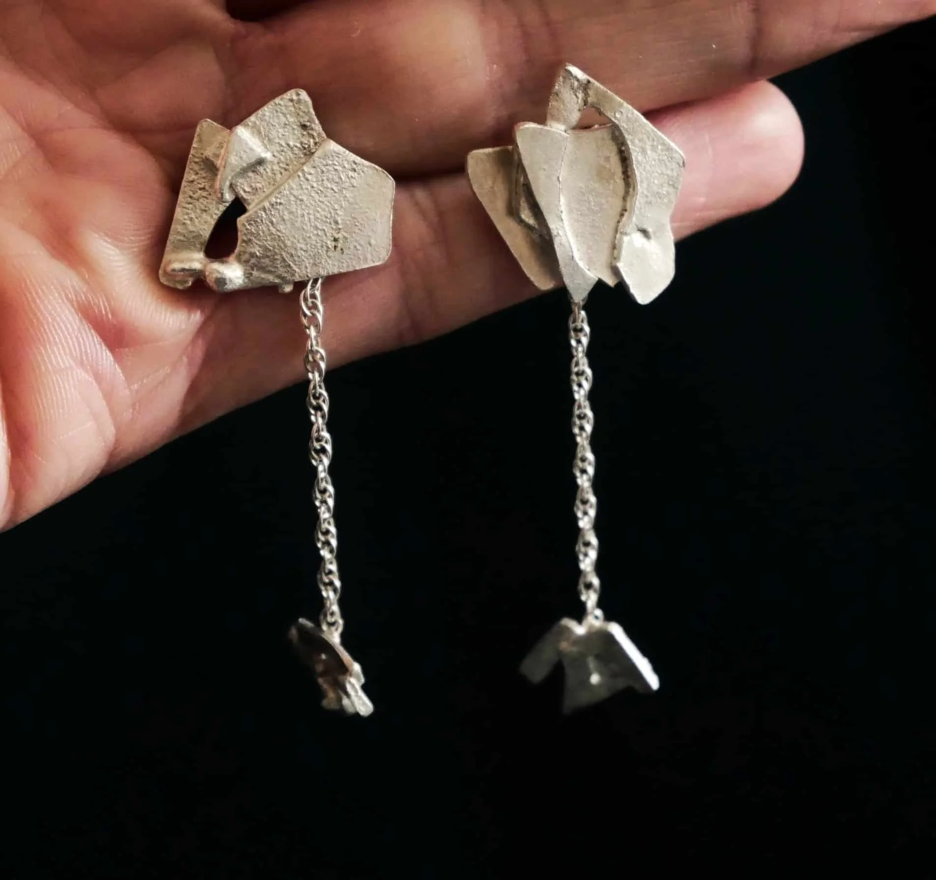 Boucles d'oreilles pendantes en argent recyclé sur fond noir. 
