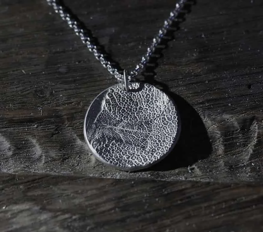 collier empreinte truffe de chien posé sur l’établi de la bijoutière. Ce pendentif truffe de chien est en argent massif 925 avec des finitions mates. Ici, l’empreinte du museau du chien ne recouvre pas tout le médaillon, c’est une demande sur mesure.