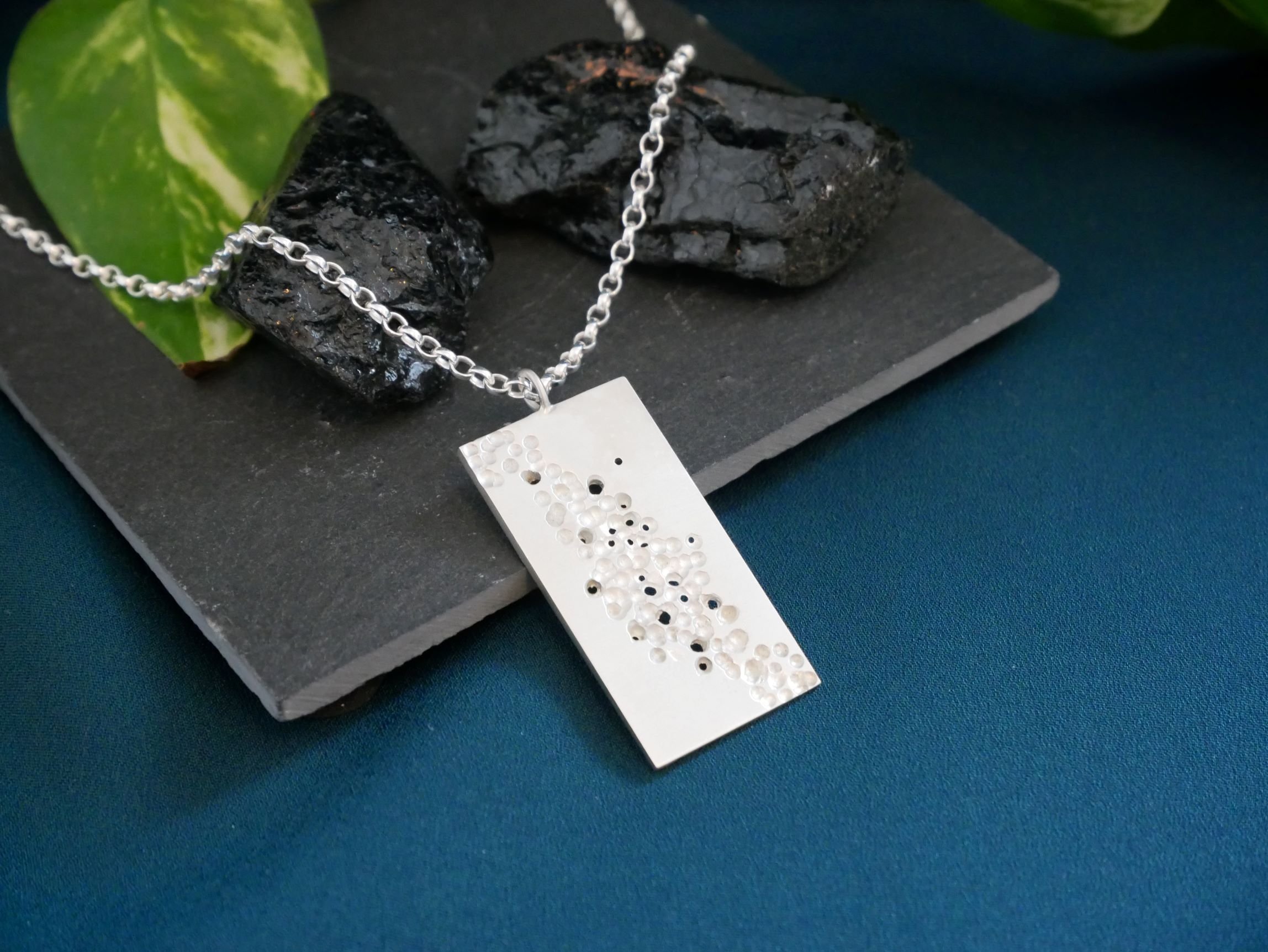 Collier rectangulaire ajouré en argent texturé, sur ardoise fond bleuté. Design contemporain, parfait pour un style audacieux avec effets de texture.