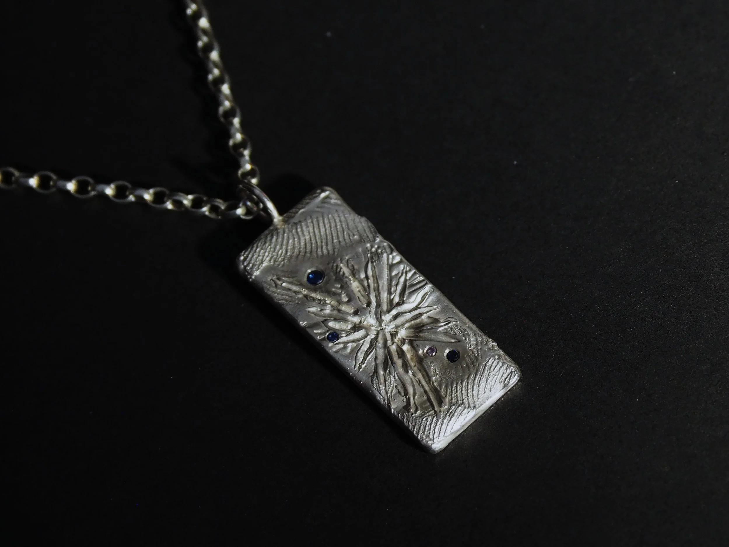 Pendentif saphirs moderne pour homme, à la forme rectangulaire, qui joue sur des effets de matière.