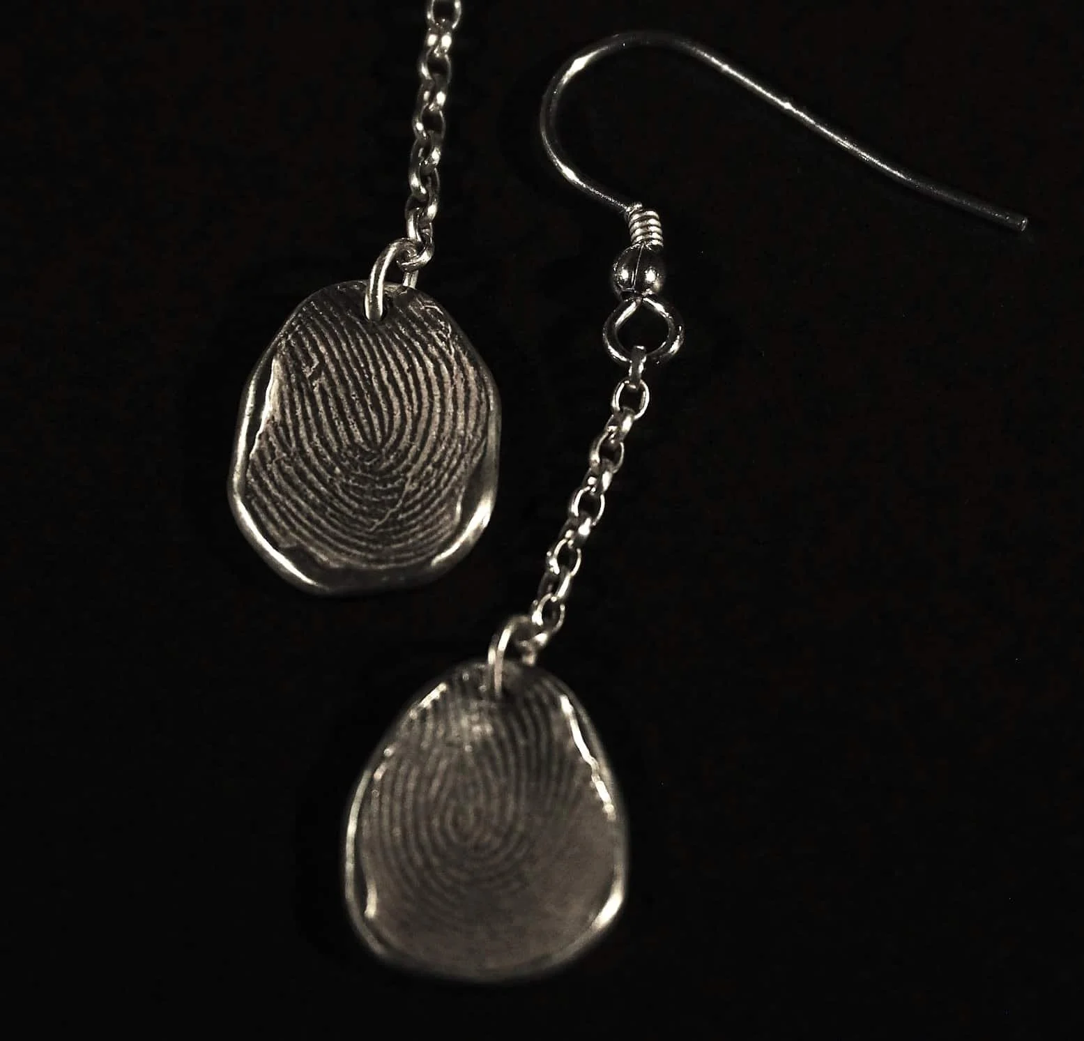 Boucles d'oreilles avec des empreintes digitales sur fond noir. 