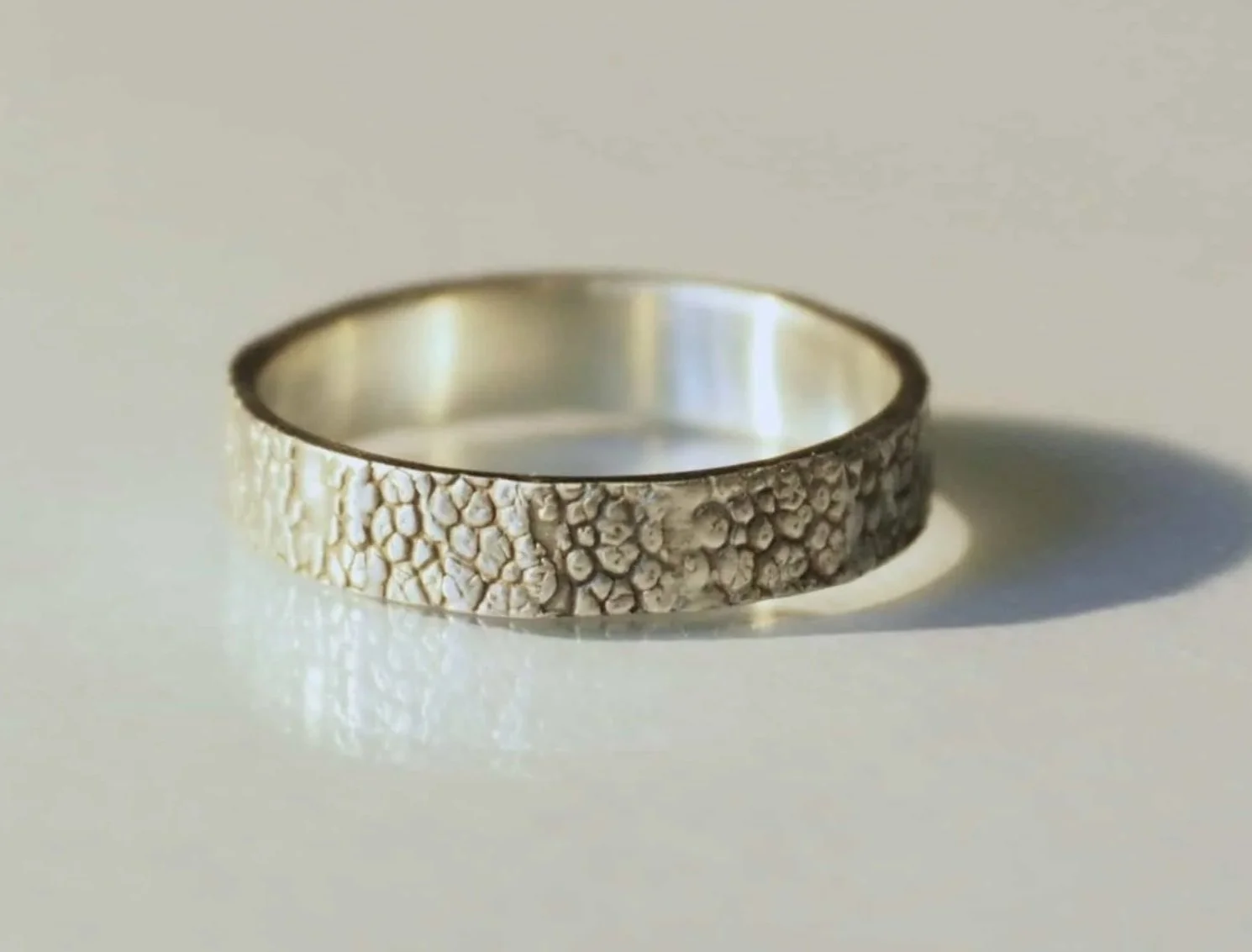 Une bague lumineuse posée sur une surface blanche révèle un motif de truffe gravé tout autour. Bague empreinte truffe chien élégante et raffinée, création sur mesure alliant émotion et savoir faire artisanal.