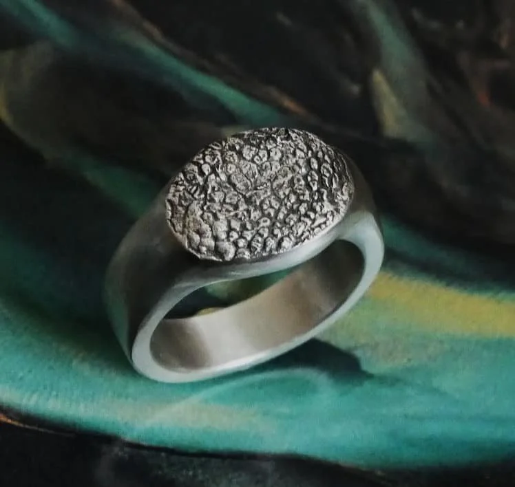 bague empreinte truffe de chien sur un fond coloré. Cette bague truffe est une chevalière en argent avec des finitions mates. L’empreinte du museau du chien est apposée sur le plateau de la chevalière.
