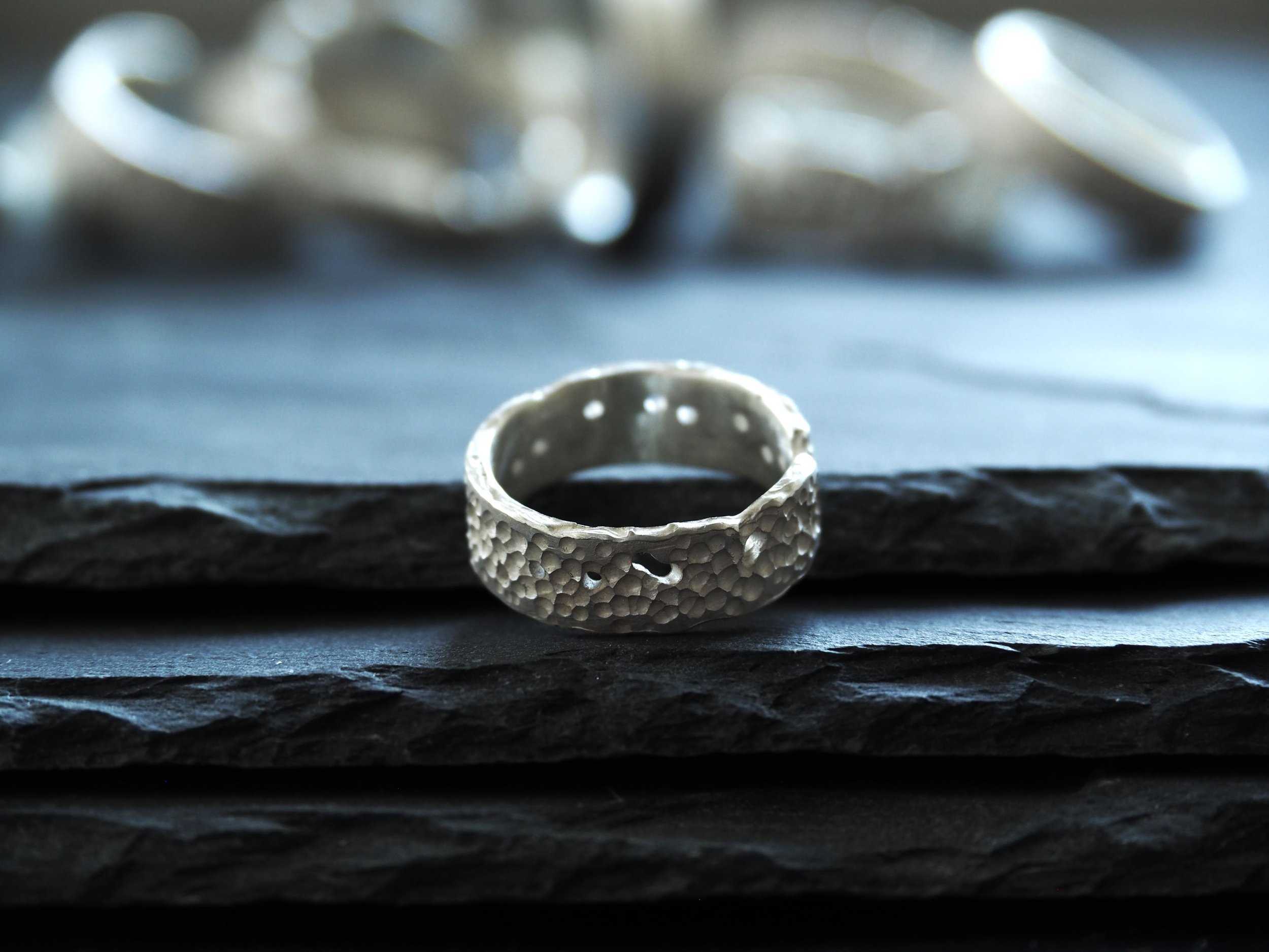 Bague en argent ajourée, anneau texturé reposant sur ardoises. Élégance brute et contemporaine avec des effets perforés, idéale comme bague originale de créateur pour un look affirmé.