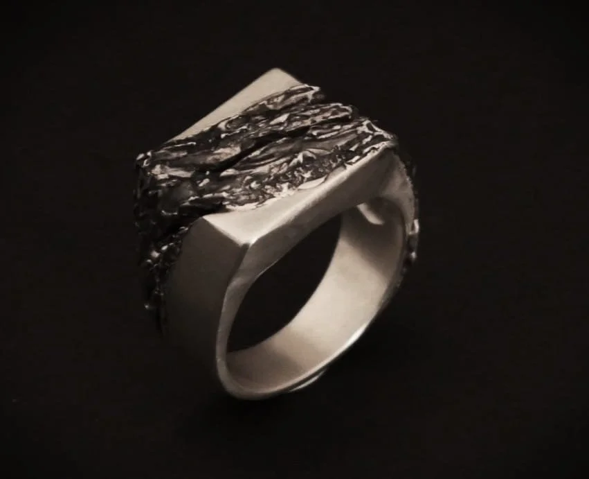 Chevalière en argent avec un jeu de texture sur le plateau sur fond noir.
