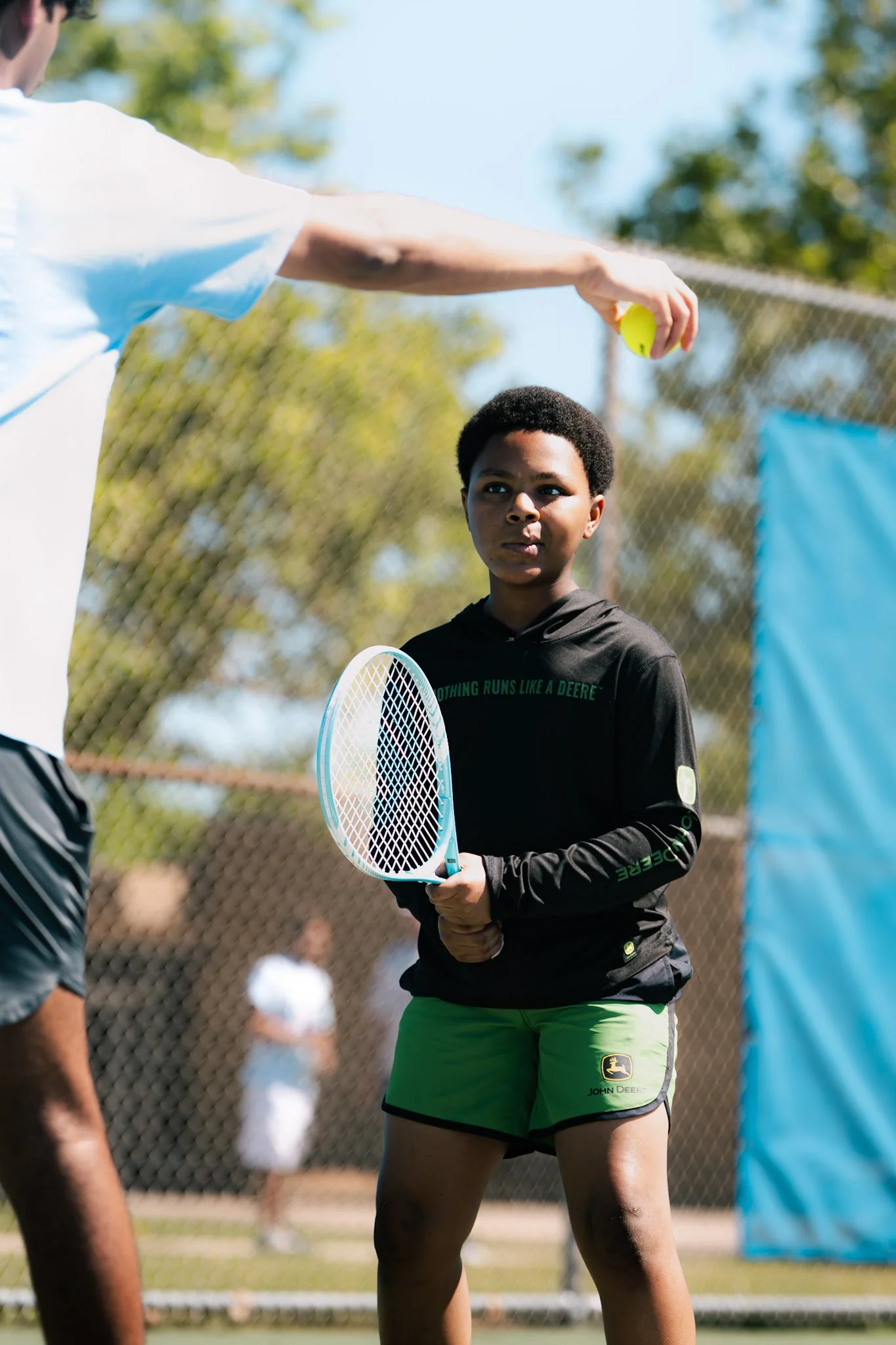 coach holding tennis ball while student watches