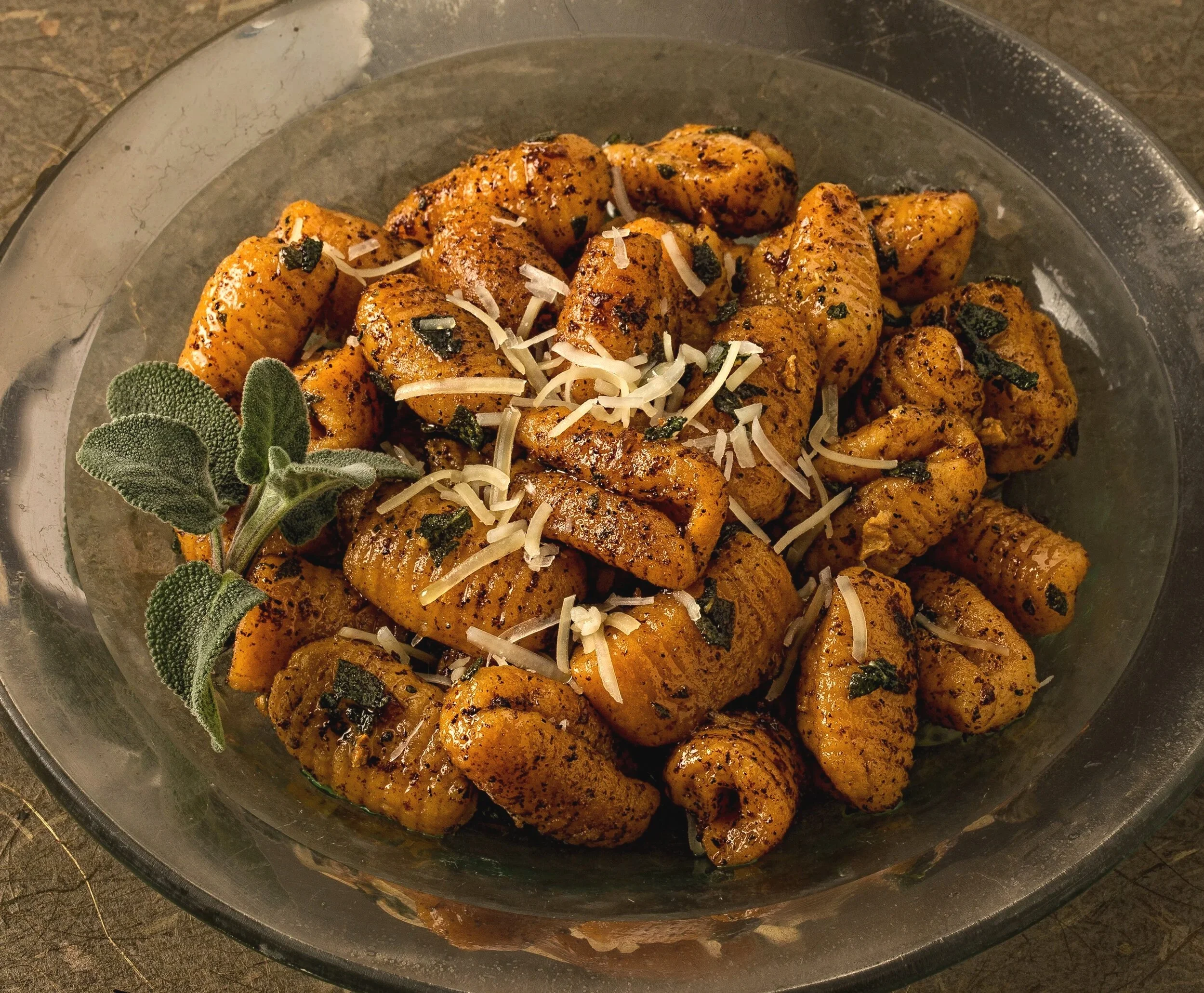 Ground chicken pieces seasoned with spices, topped with shredded cheese and fresh sage leaves in a glass dish.