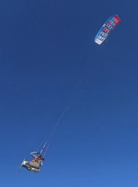 Person paragliding with a red, blue, and white parachute in a clear blue sky.