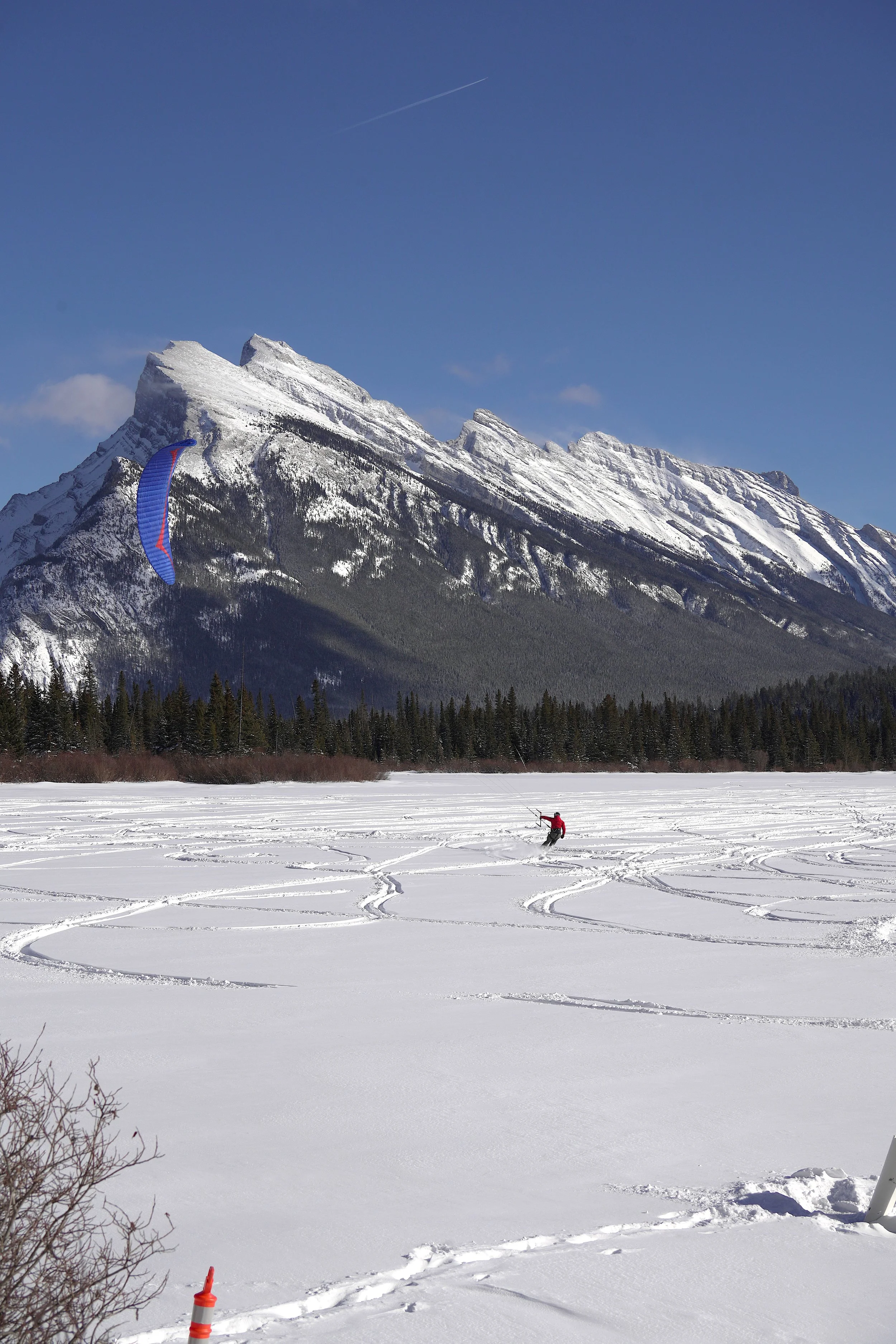 A person snowboarding on a snowy field with a mountain in the background and a blue sky above. Vermillion Lakes. Banff National Park. 