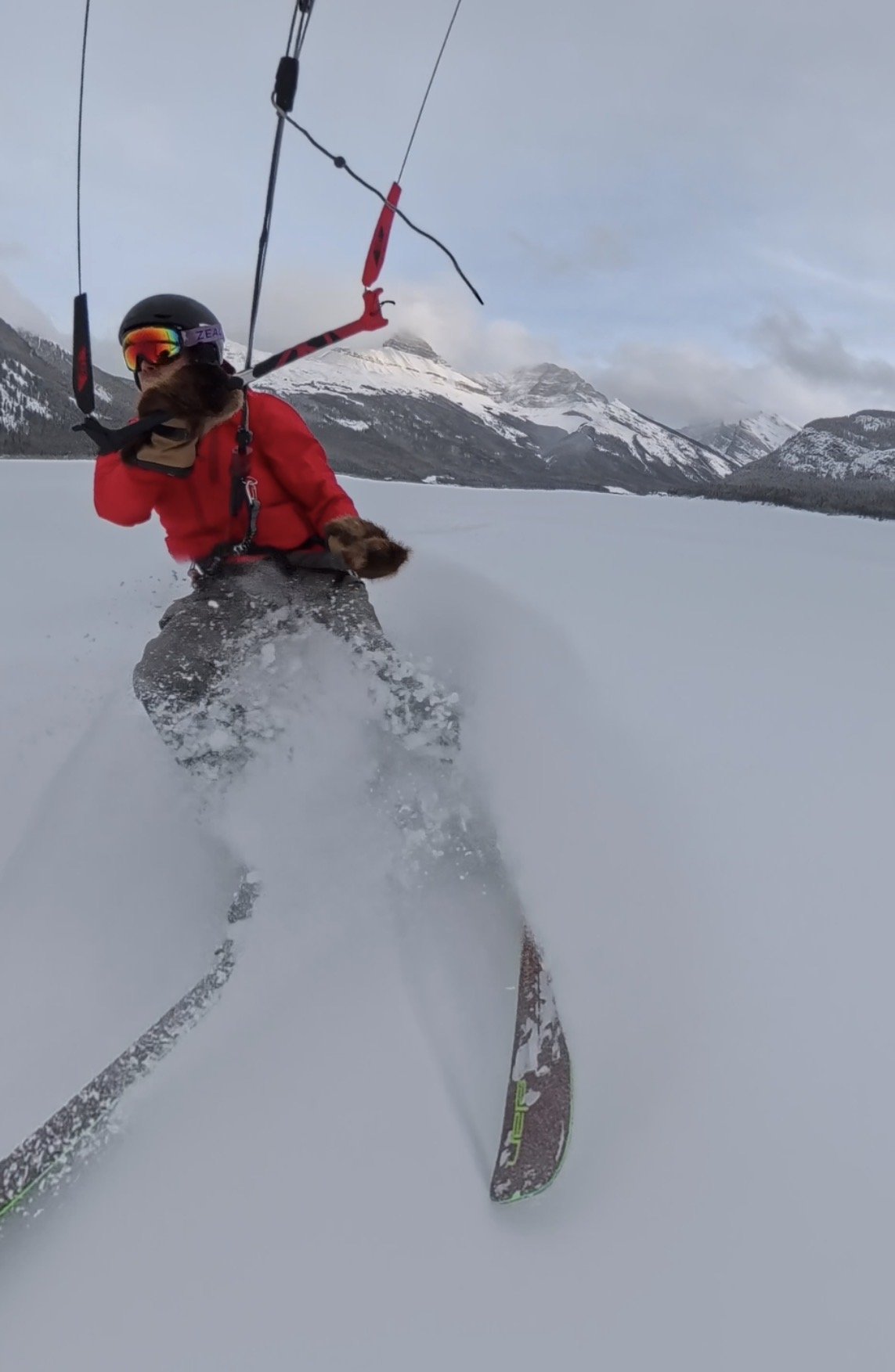 Person in red jacket and helmet snowboarding on snow-covered landscape with mountains in the background.