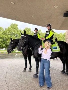 Founder and Registered Physiotherapist of Peace of Mind CBT, Alison Pereira, is standing in front of two mounted police officers in Burlington.