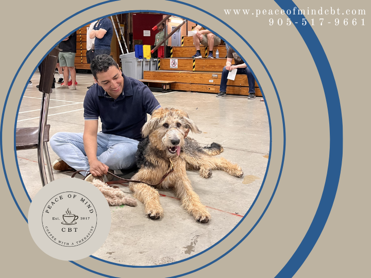 Peace of Mind CBT Therapy Dog, River, is lying beside a First Responder who is smiling and petting him.