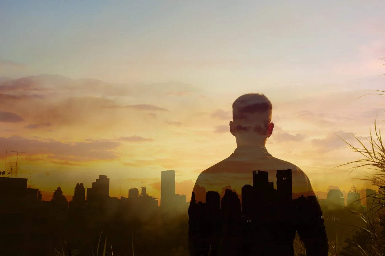 Faded silhouette of a man overlooking a city as the sunsets.
