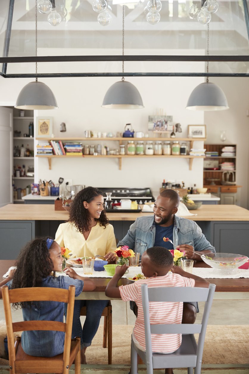Family of four sitting at their dinner table by the kitchen, talking and laughing.