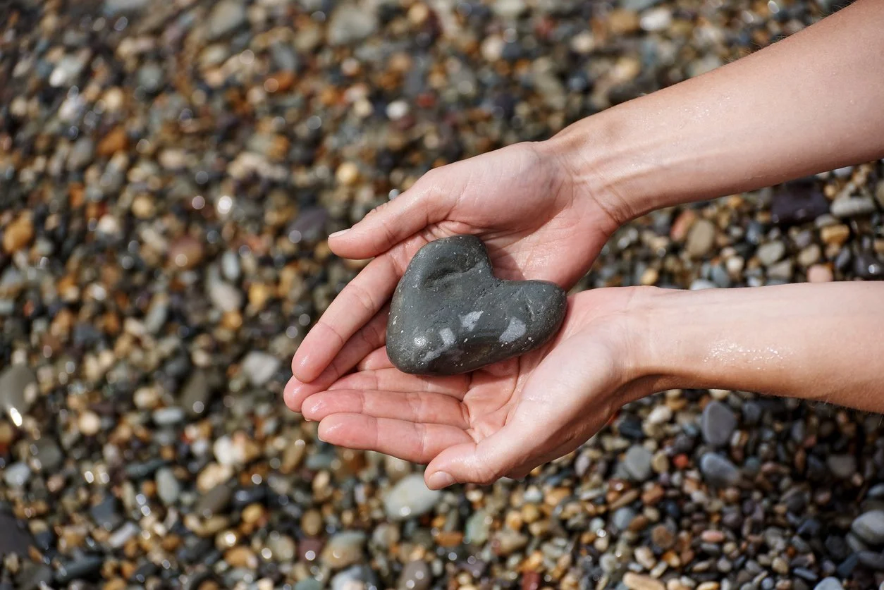 Hands holding a rock in the shape of a heart.
