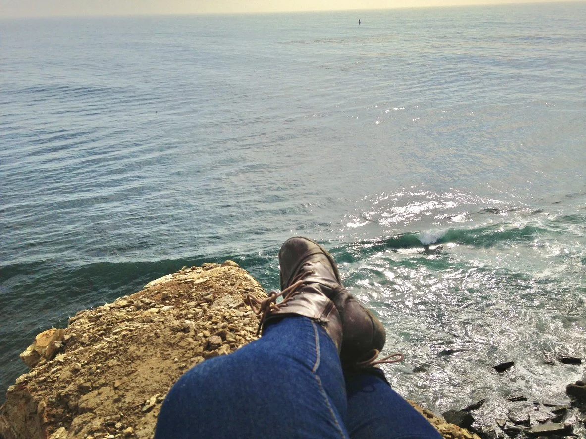 Crossed legs of a woman sitting on a rock overlooking a lake on a sunny day.