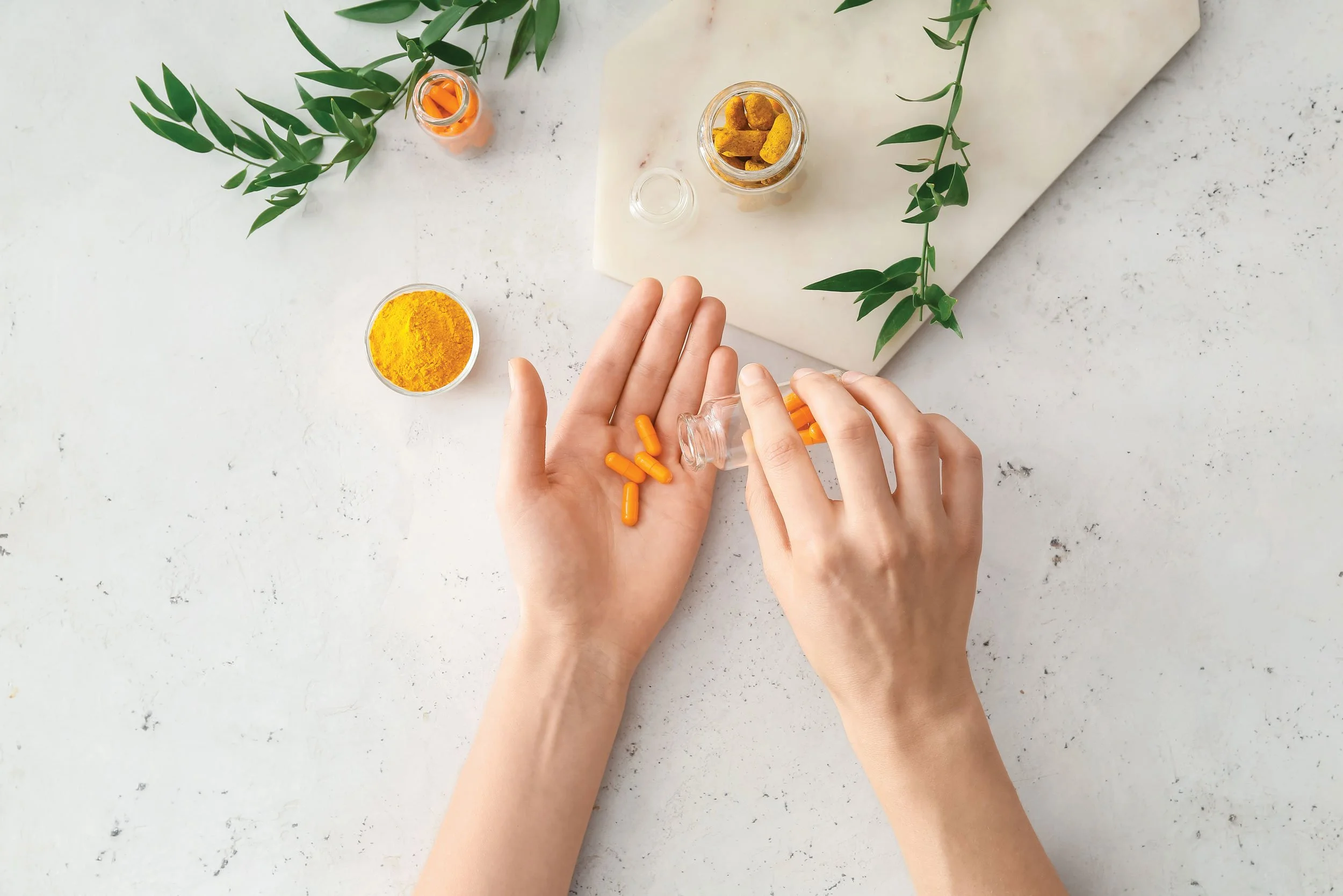 Hands at a kitchen bench with opened supplement capsules and fresh herbs, illustrating practitioner-only supplements