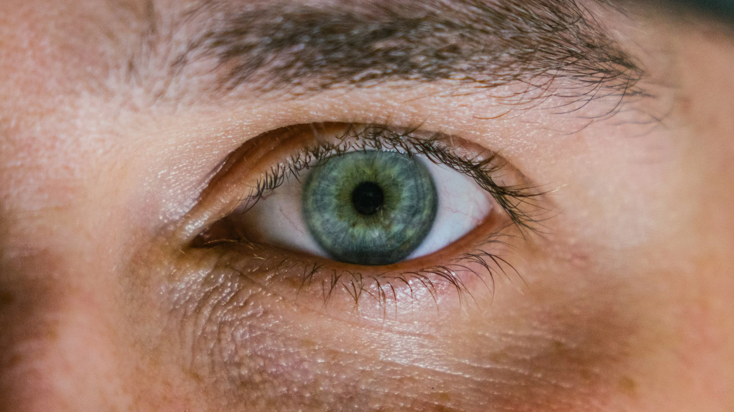 Close-up of a human eye with a blue-green iris, brown eyelashes, and skin details.