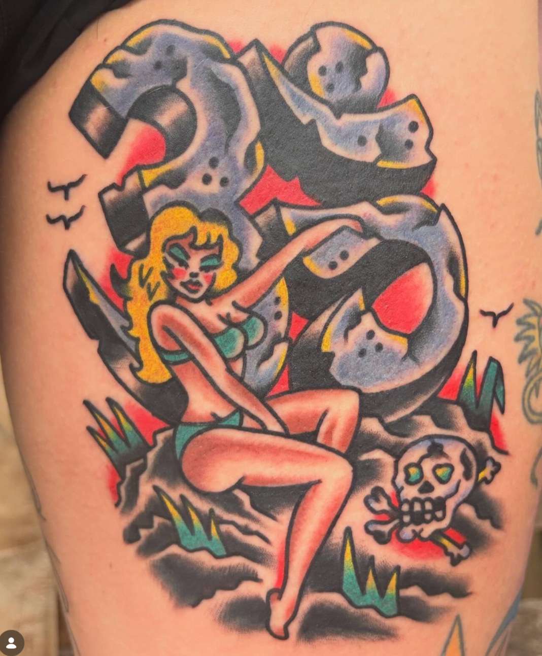 Colorful tattoo of a mythical creature with a lion's face, human body, wings, and horns, holding a skull, with vibrant colors and bold lines.